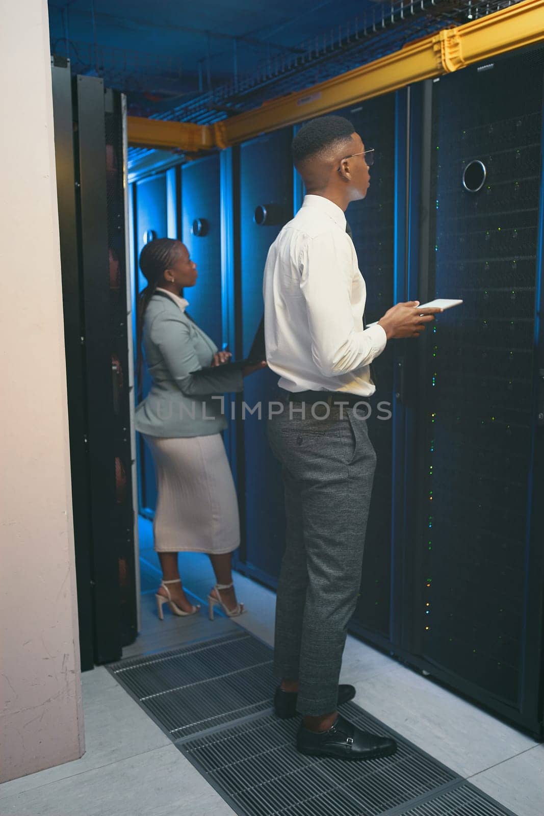 The system shouldnt be running at this pace. Full length shot of two young IT specialists standing together in the server room and using technology. by YuriArcurs
