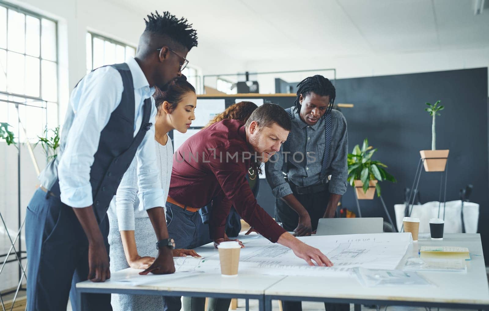 Lets do the maths here...a team of professionals working on blueprints in an office. by YuriArcurs