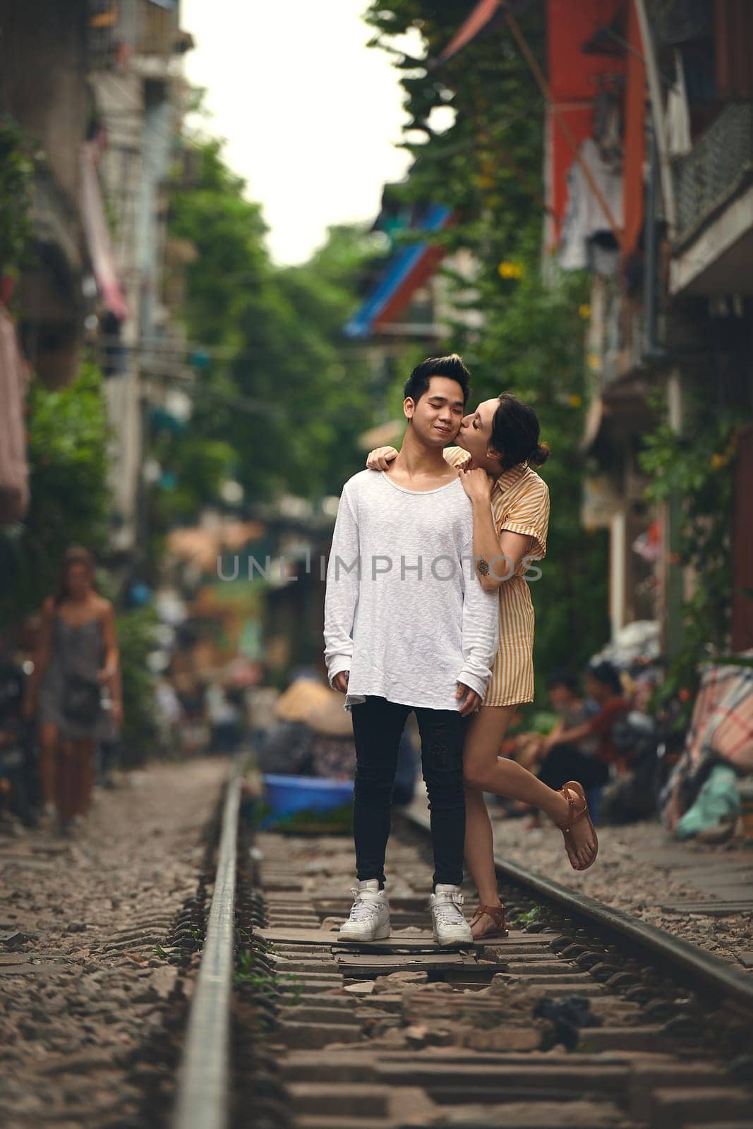 Her kisses make my heart smile. a young couple sharing a romantic moment on the train tracks in the streets of Vietnam. by YuriArcurs