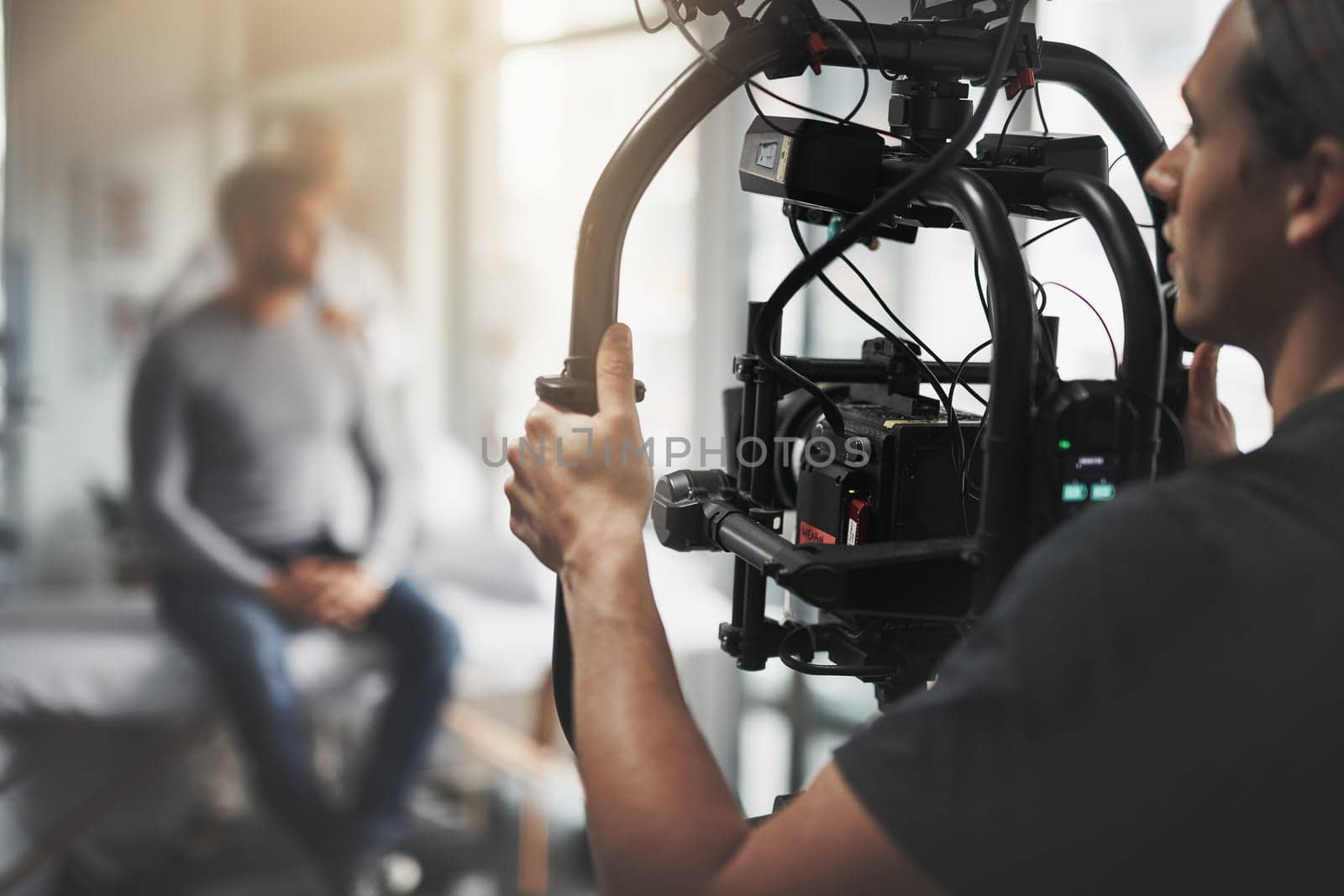 Doing it cinematic style. Behind the scenes shot of a camera operator shooting a scene with a state of the art camera inside of a studio during the day. by YuriArcurs