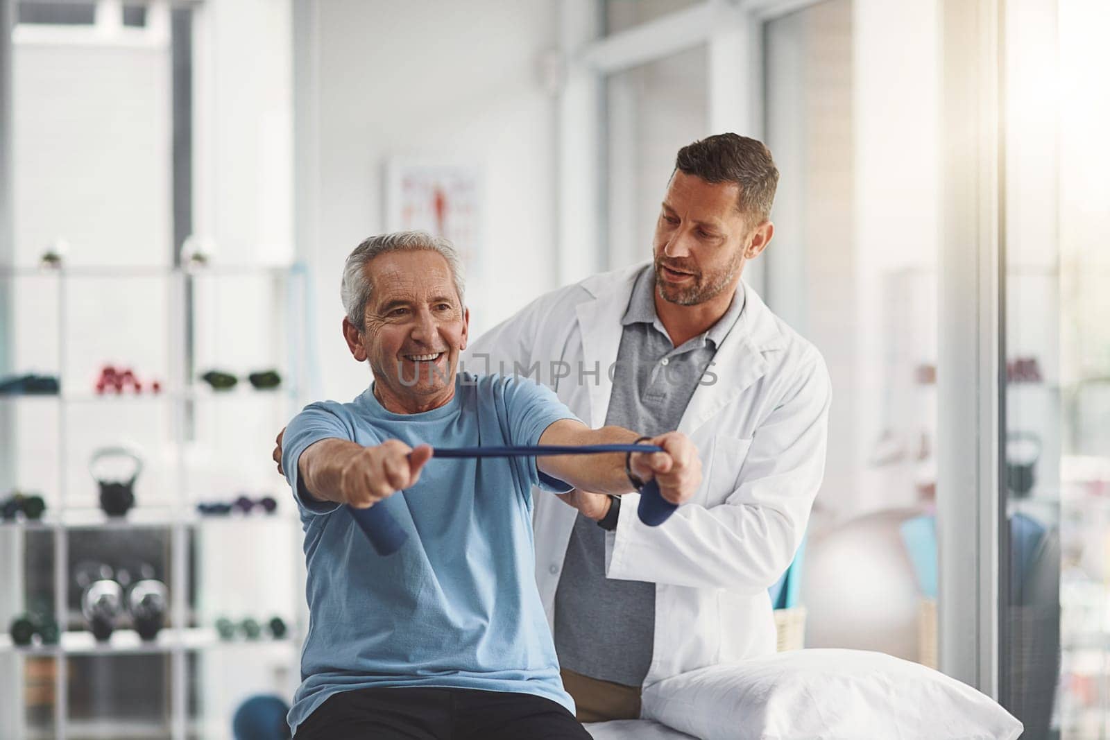 His strength and happiness grows with each day. a young male physiotherapist assisting a senior patient in recovery. by YuriArcurs