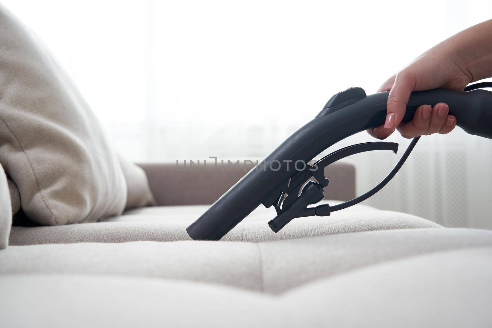 Young housewife Cleaning the Sofa with Vacuum Cleaner in living room