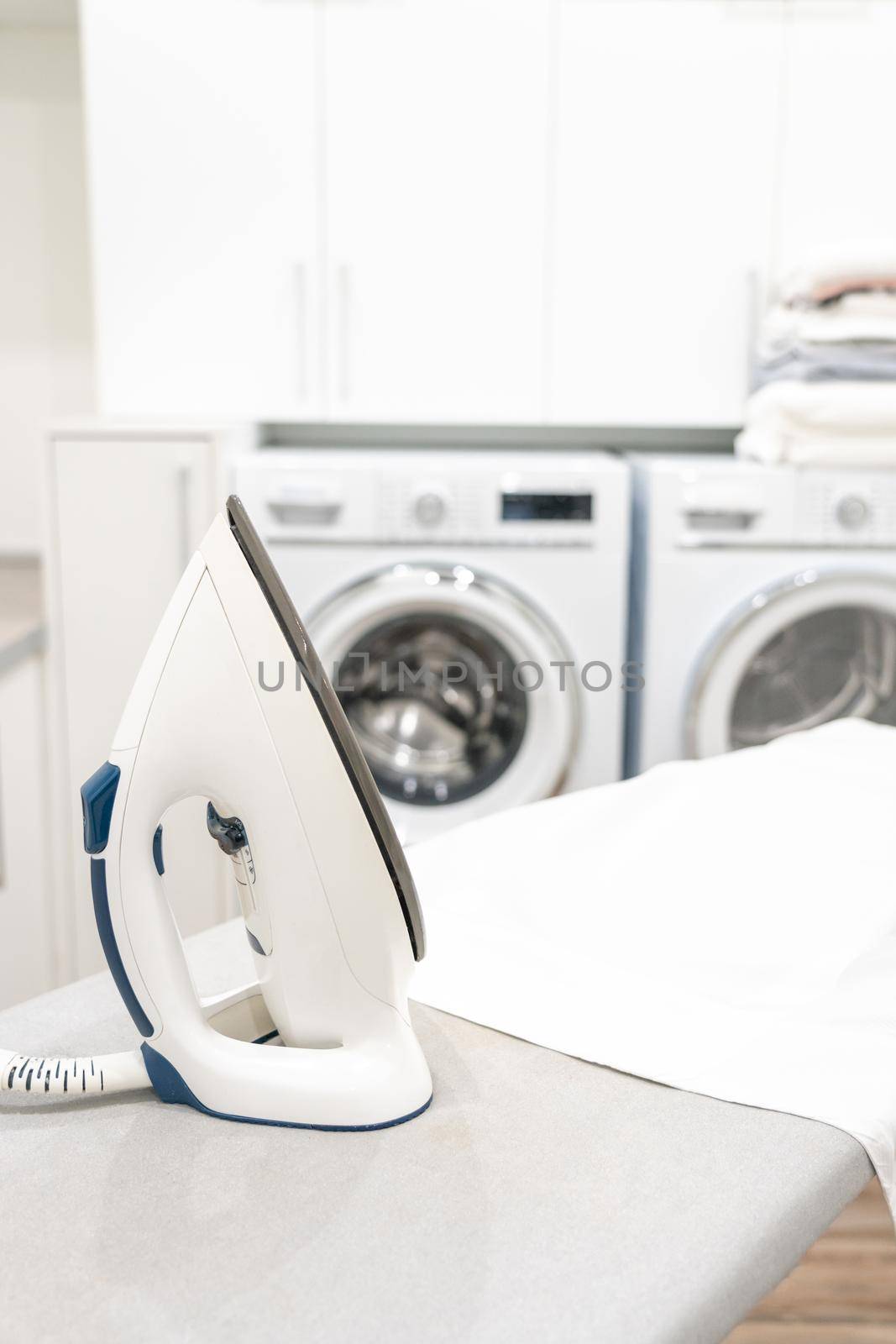 Iron on ironing board with white shirt in modern laundry room