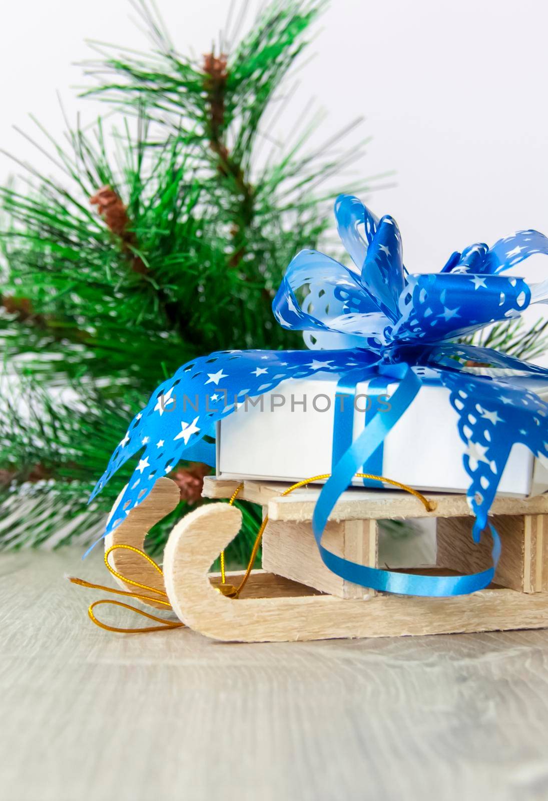 A Christmas gift with a large blue bow is lying on a wooden sleigh. Happy New year and merry Christmas. Christmas greeting card. 