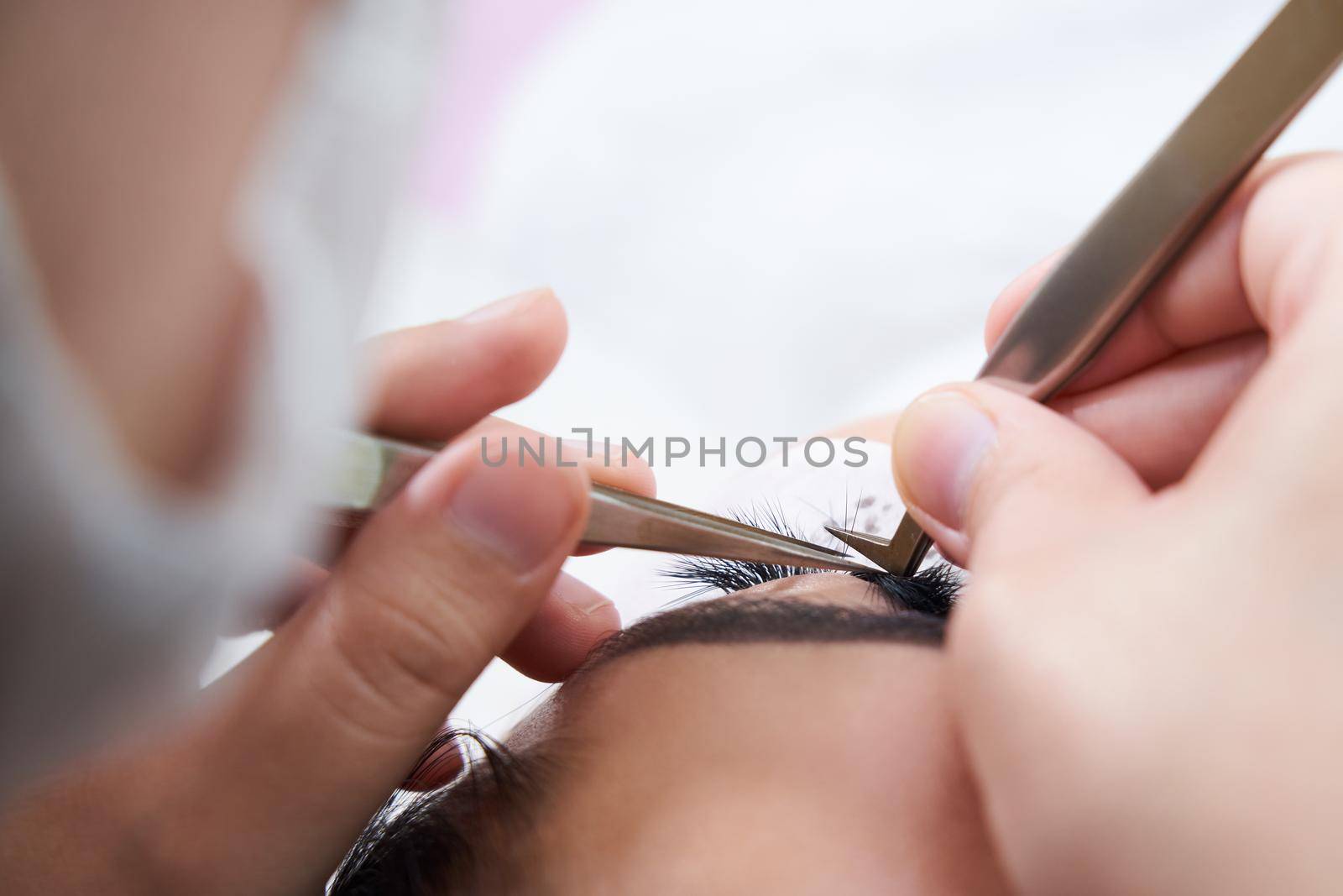 Eyelash extension procedure with tweezers in a beauty salon