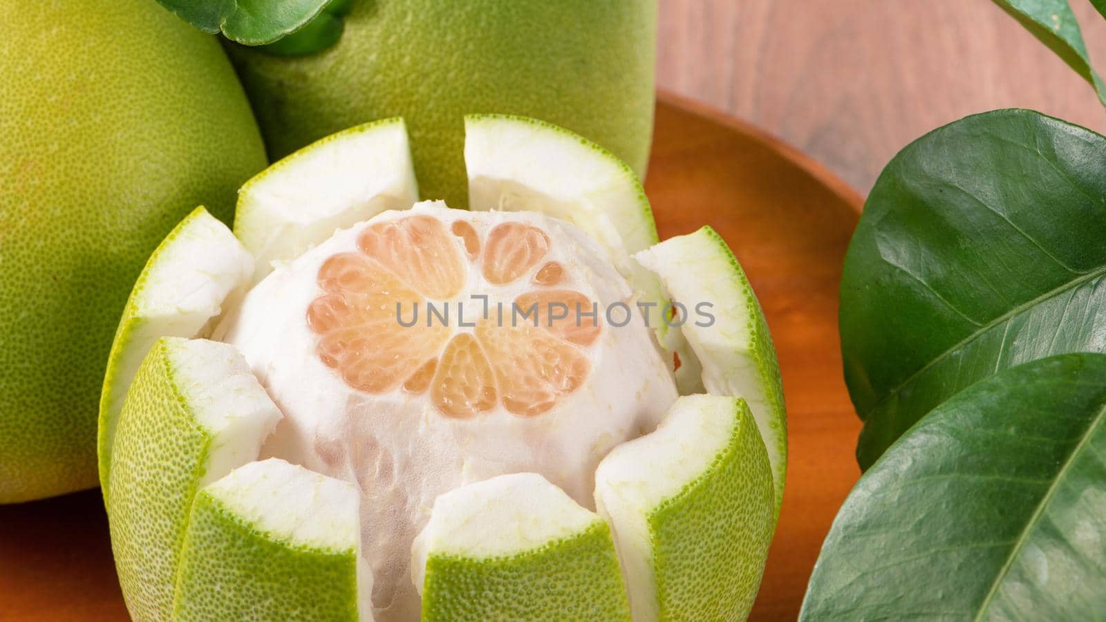 Fresh peeled pomelo, grapefruit, shaddock with green leaves on dark wooden plank table. Seasonal fruit near mid-autumn festival, close up, copy space