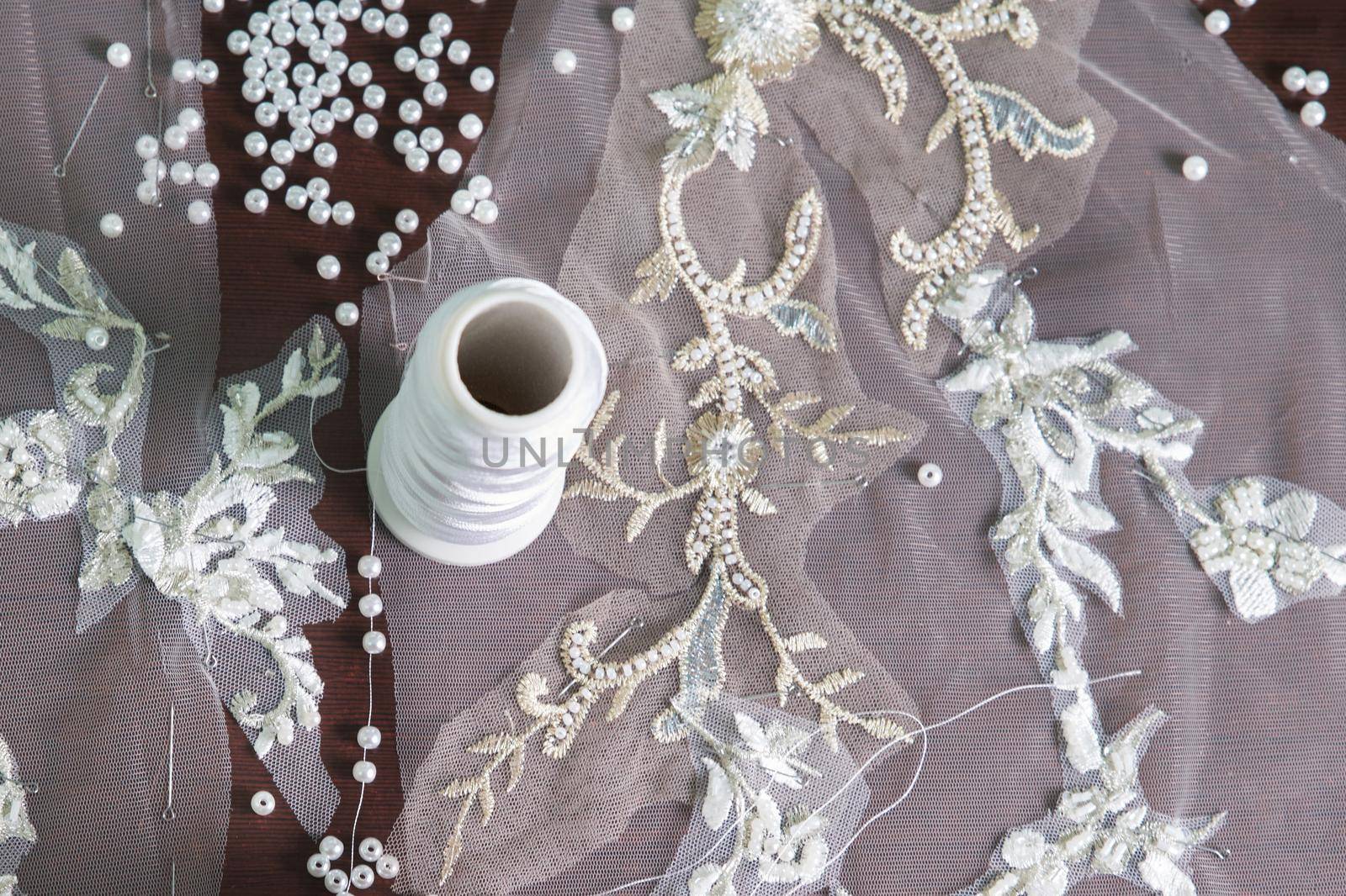 close-up of female hands of seamstress tailor sewing wedding dress using beads and lace in the studio