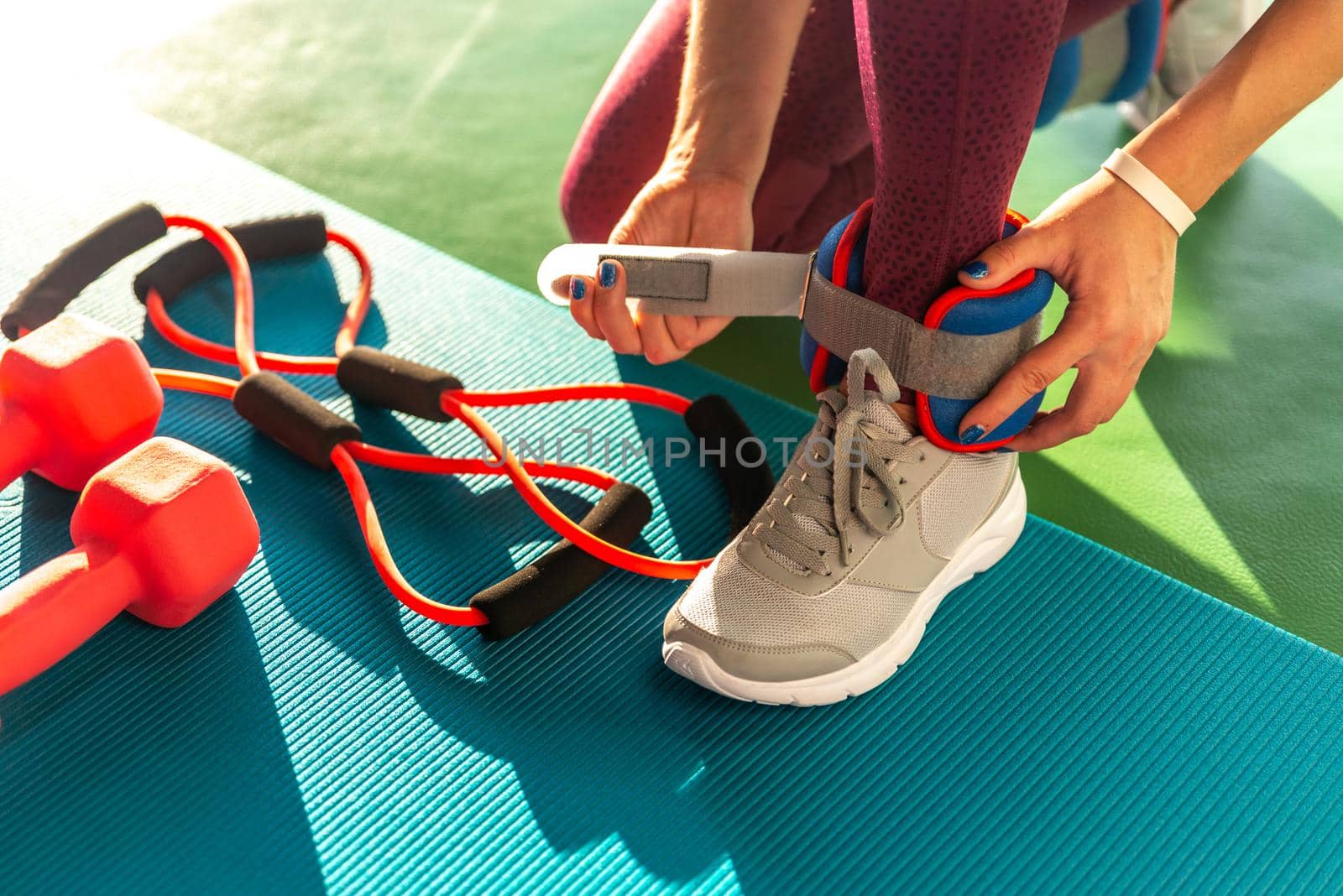 Woman putting on ankle wights before she starts a workout in a gym, health and fitness