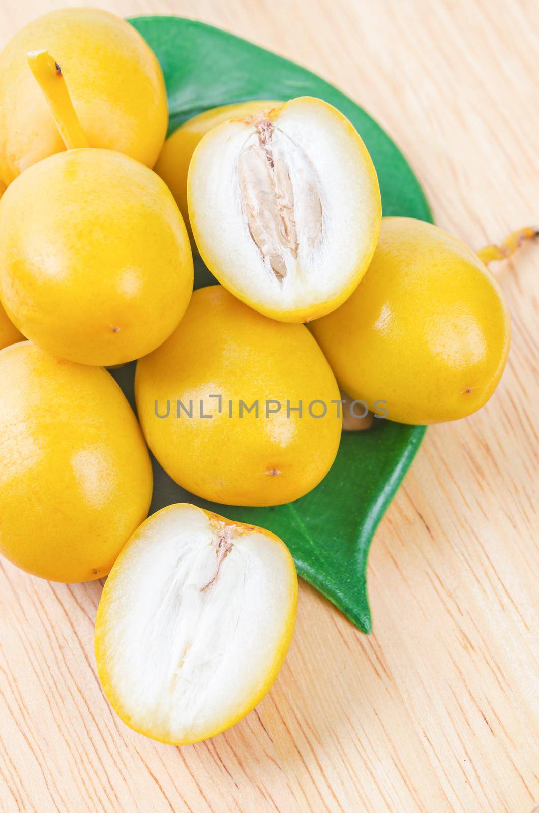 Fresh date palm fruits with green leaf on wooden background.