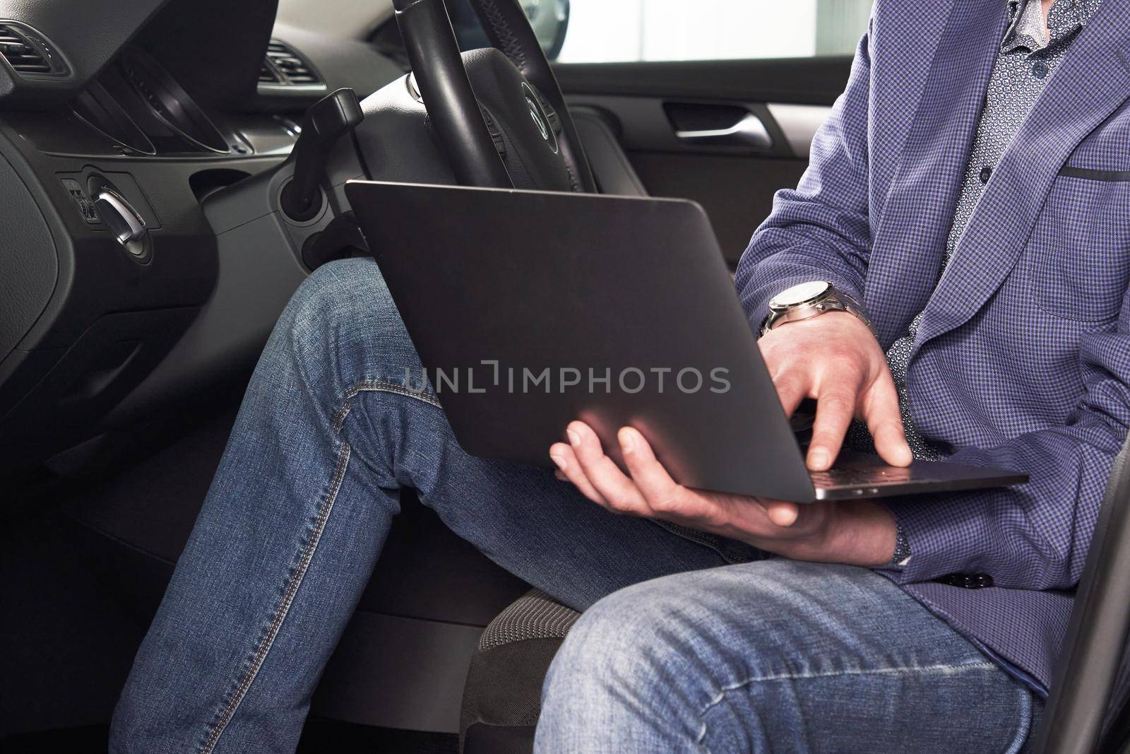 Professional man with a laptop in car tunes tuning control system, updating software, gaining access through to computer, sitting in cabin