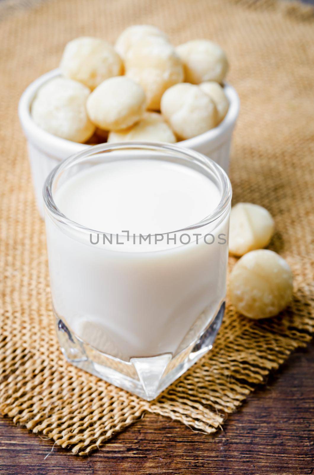 Macadamia milk in a glass and a bowl of macadamia nuts. by Gamjai