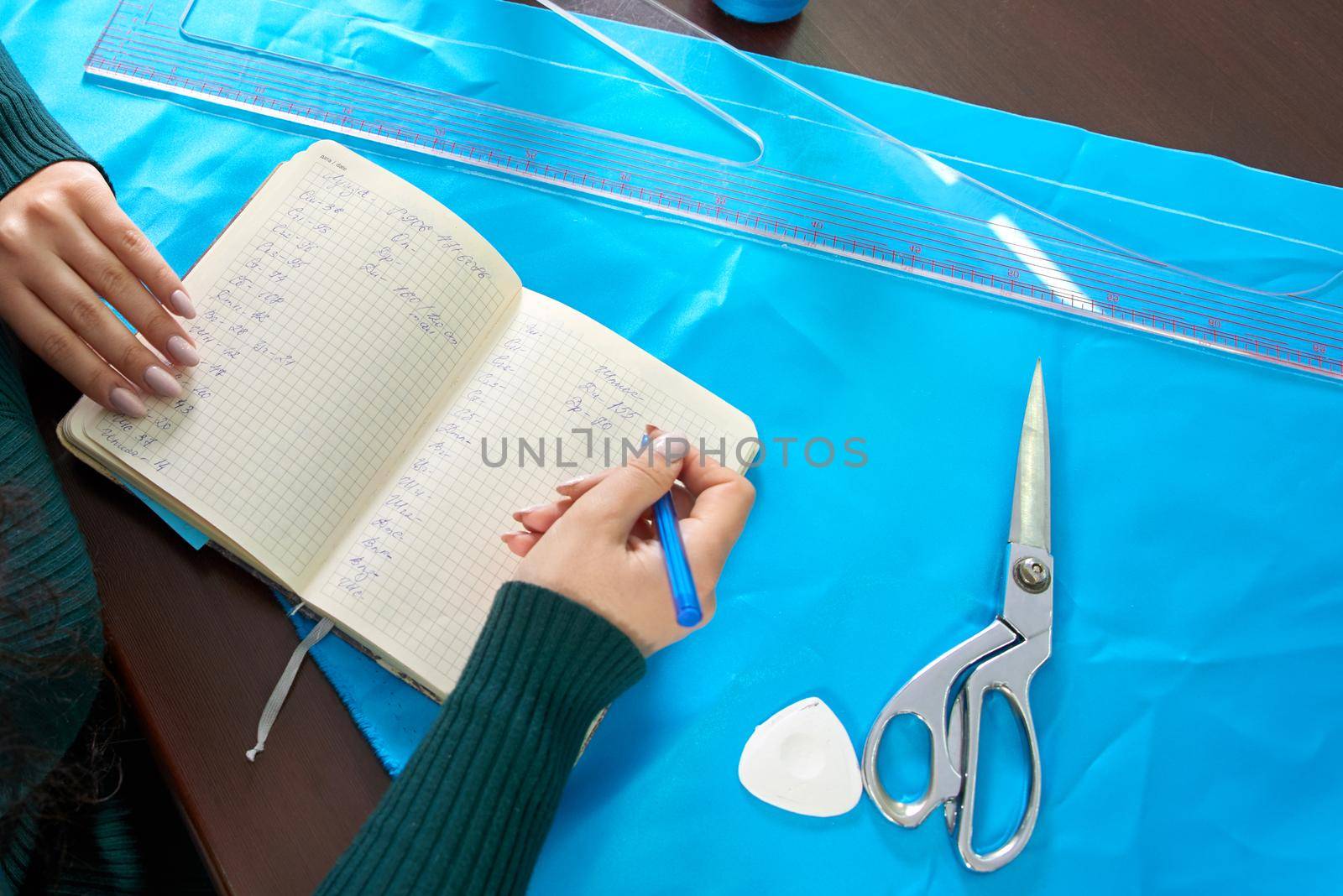 beautiful seamstress with long hair writes in a notebook. the tailor creates a collection of outfits. young woman designer clothes notes ideas in notebook