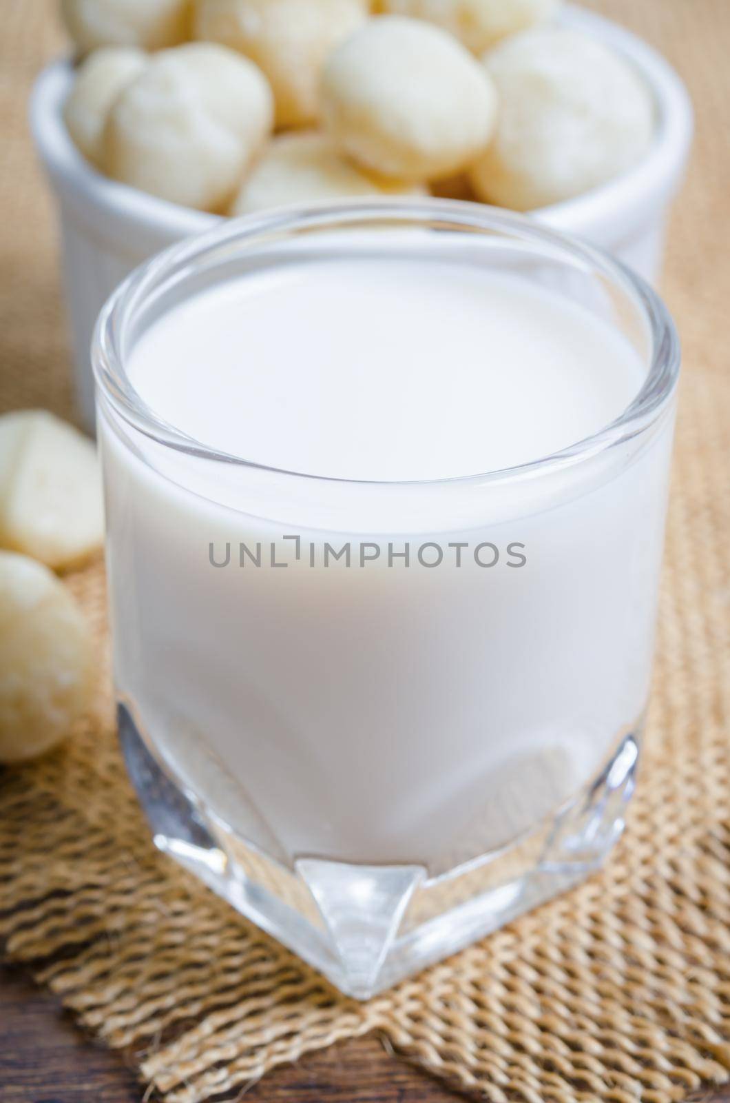 Macadamia milk in a glass and a bowl of macadamia nuts. by Gamjai