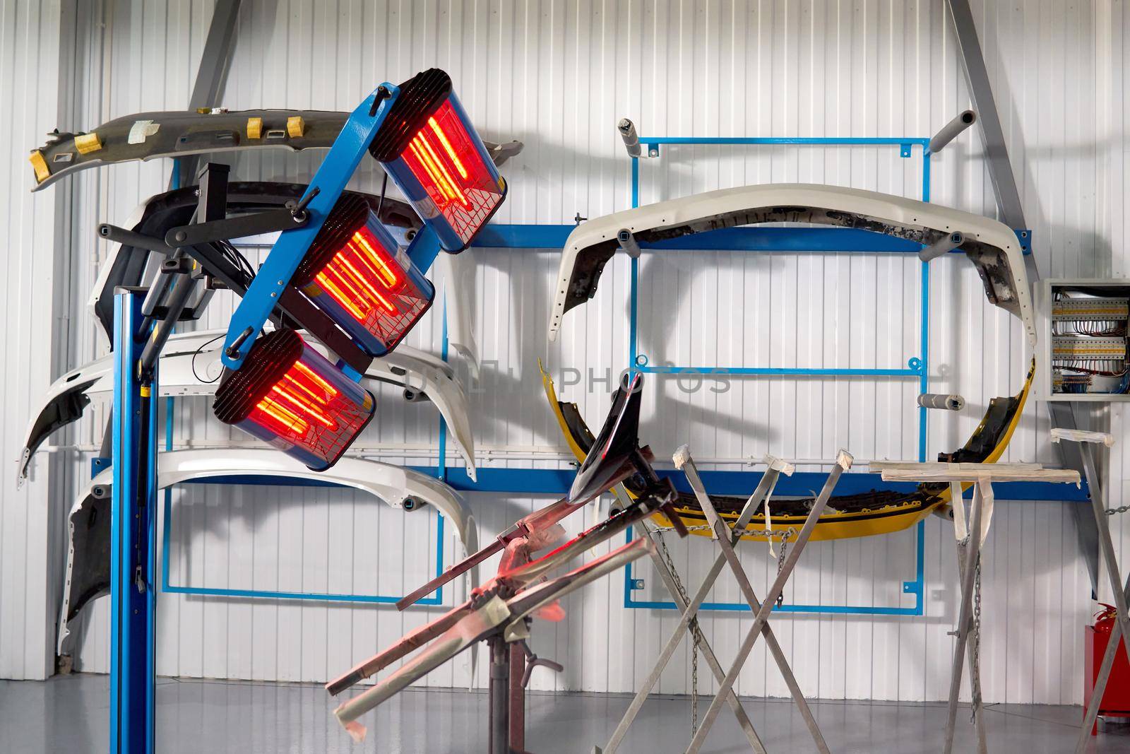 Painting and drying under lamps in professional box of car body parts after applying paint on bumper