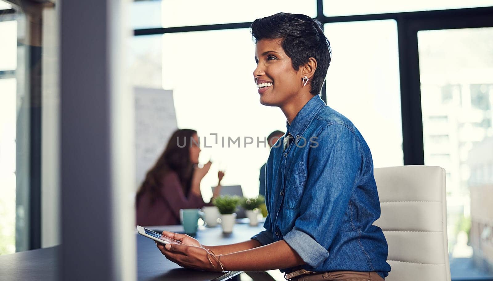 Dont doubt your dreams. a young businesswoman working on a digital tablet with her colleagues in the background. by YuriArcurs