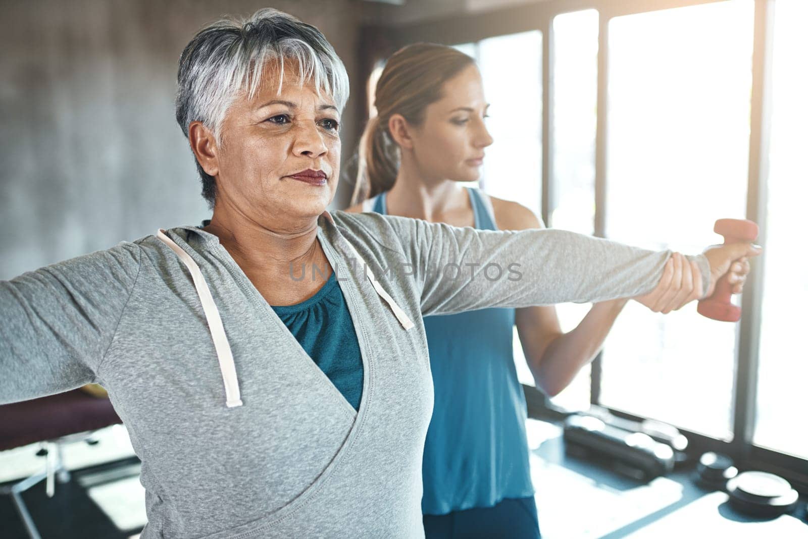 Dumbbell, physiotherapy and old woman with personal trainer for fitness, wellness or rehabilitation. Health, workout or retirement with senior patient and physiotherapist in gym for support training.