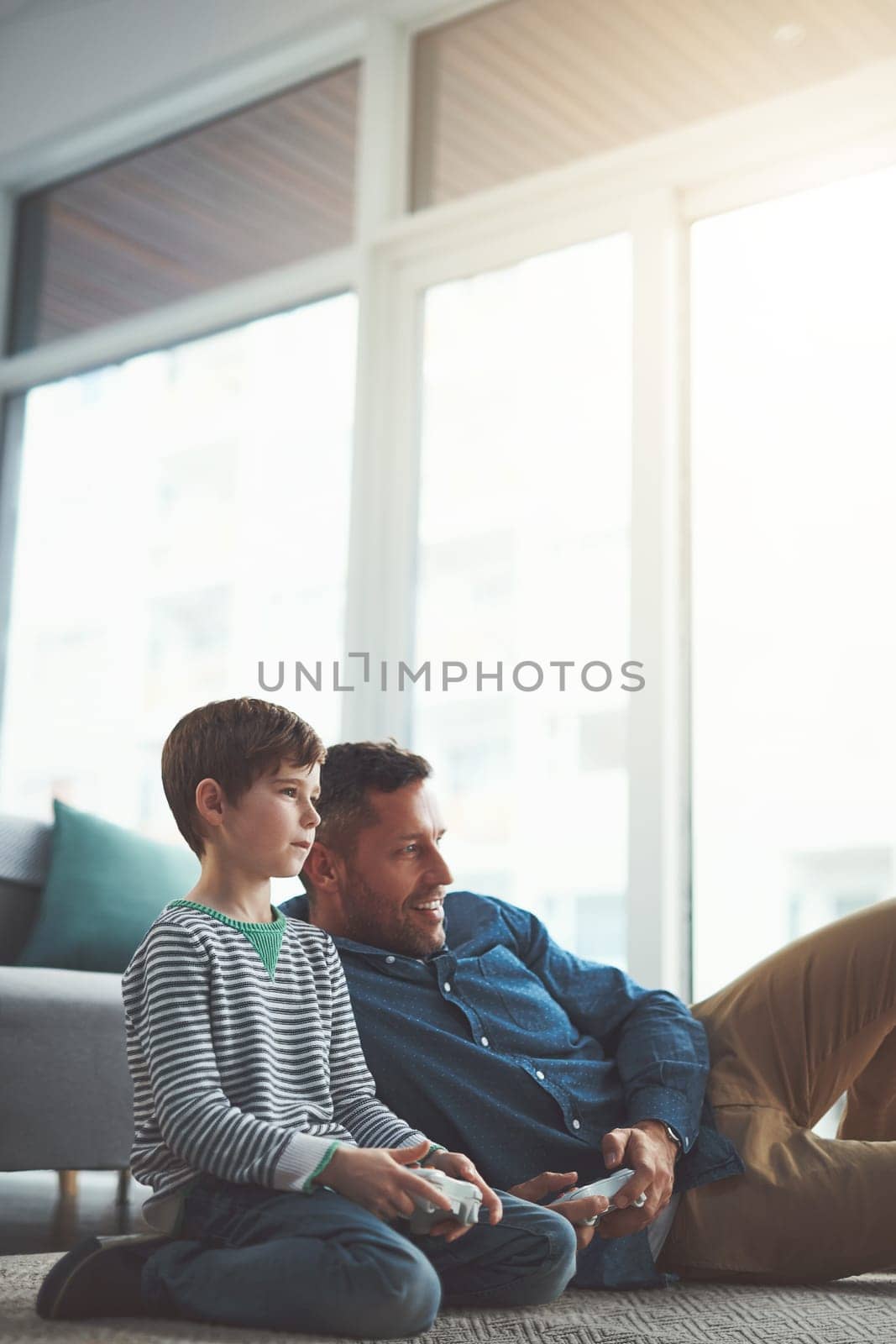 Youve gotten better dad. a cheerful little boy and his father playing video games together on the television while being seated on the floor at home during the day