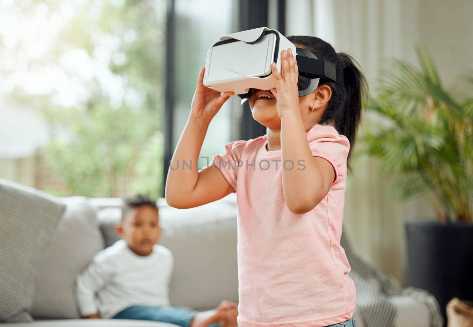 Young girl with VR goggles, gaming and metaverse with futuristic tech, child experience simulation at family home. Female kid in living room with video games, virtual reality and future technology.