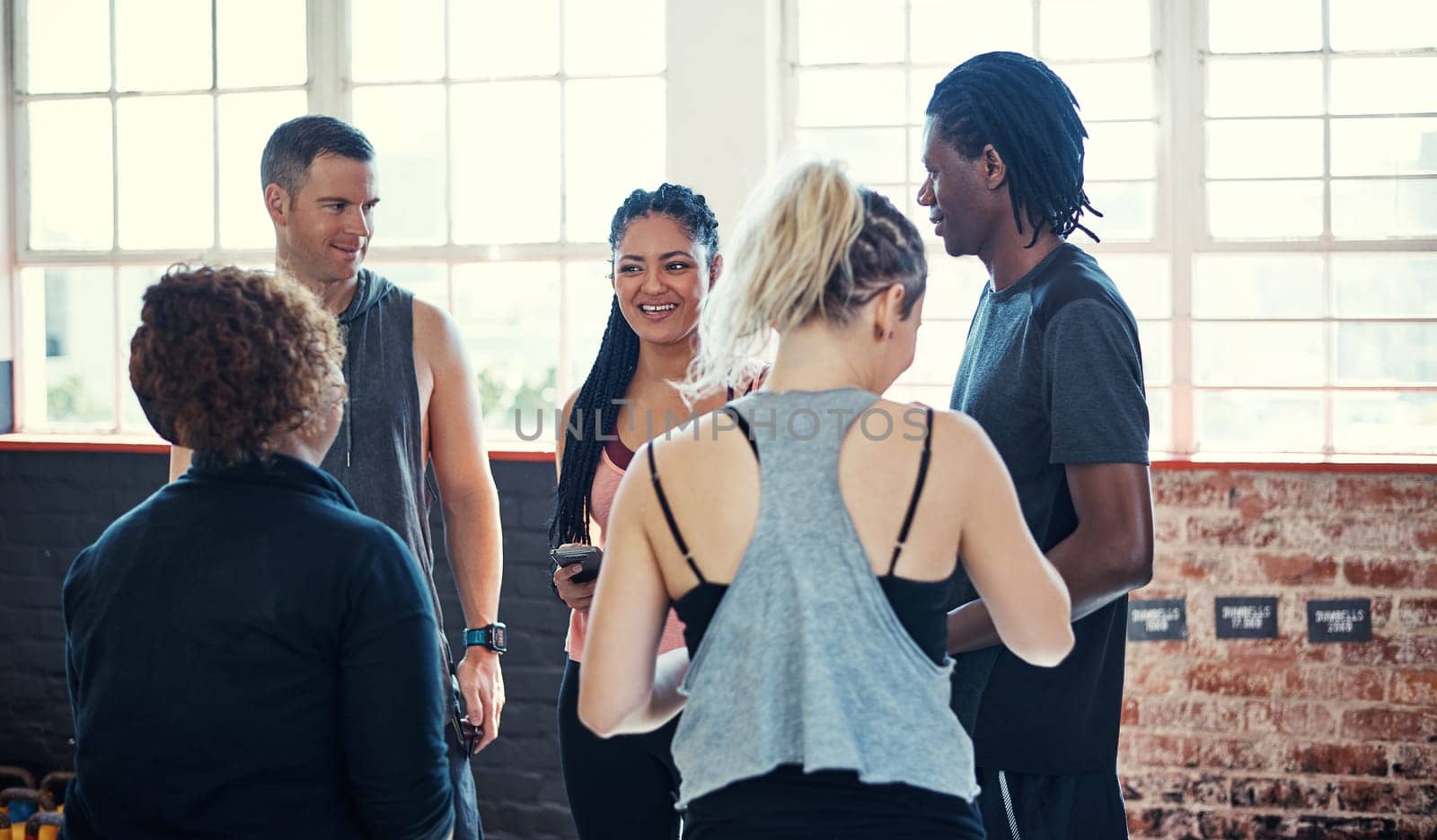 Some workout chit chat. a cheerful young group of people standing in a circle and having a conversation before a workout in a gym. by YuriArcurs