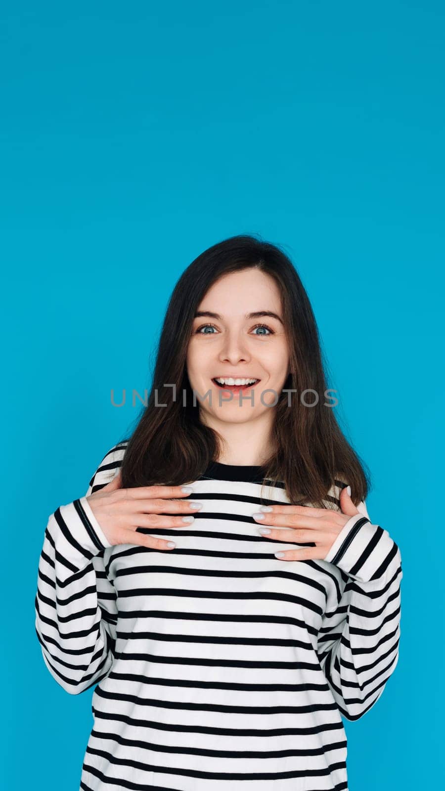Portrait of a gorgeous, pretty, imposing girl in a striped pullover with her arms across her chest, isolated on a blue background.