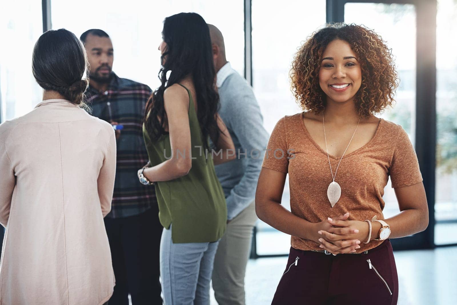 I trust my team completely. Portrait of an attractive young woman standing in the office with her colleagues in the background. by YuriArcurs