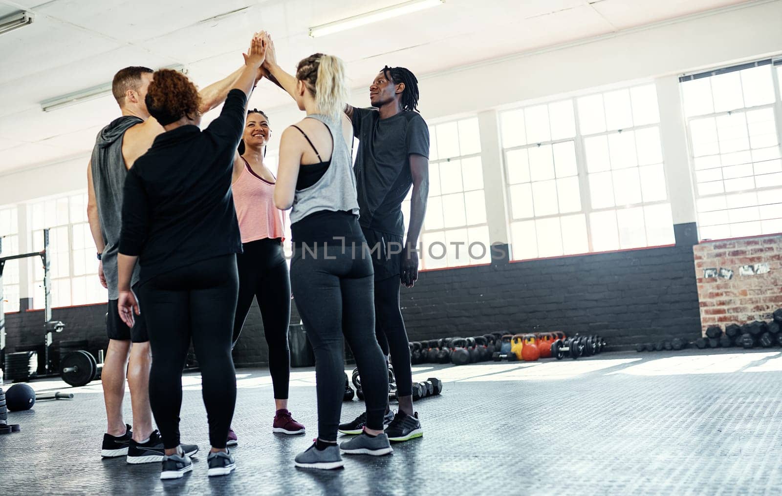 Sticking together. a cheerful young group of people forming a huddle together before a workout session in a gym. by YuriArcurs