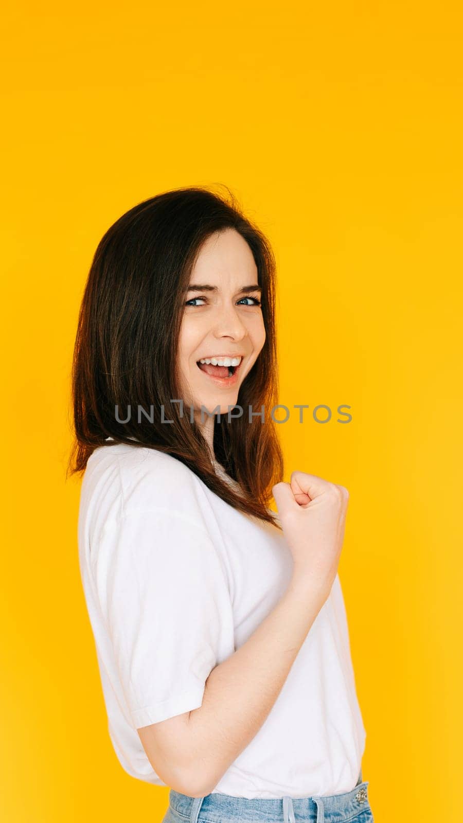 Victory Gesture: Enthusiastic Lady with Fist Raised in Triumph, Shouting in Excitement - Capturing Success, Achievement and Positive Energy Against a Yellow Background.