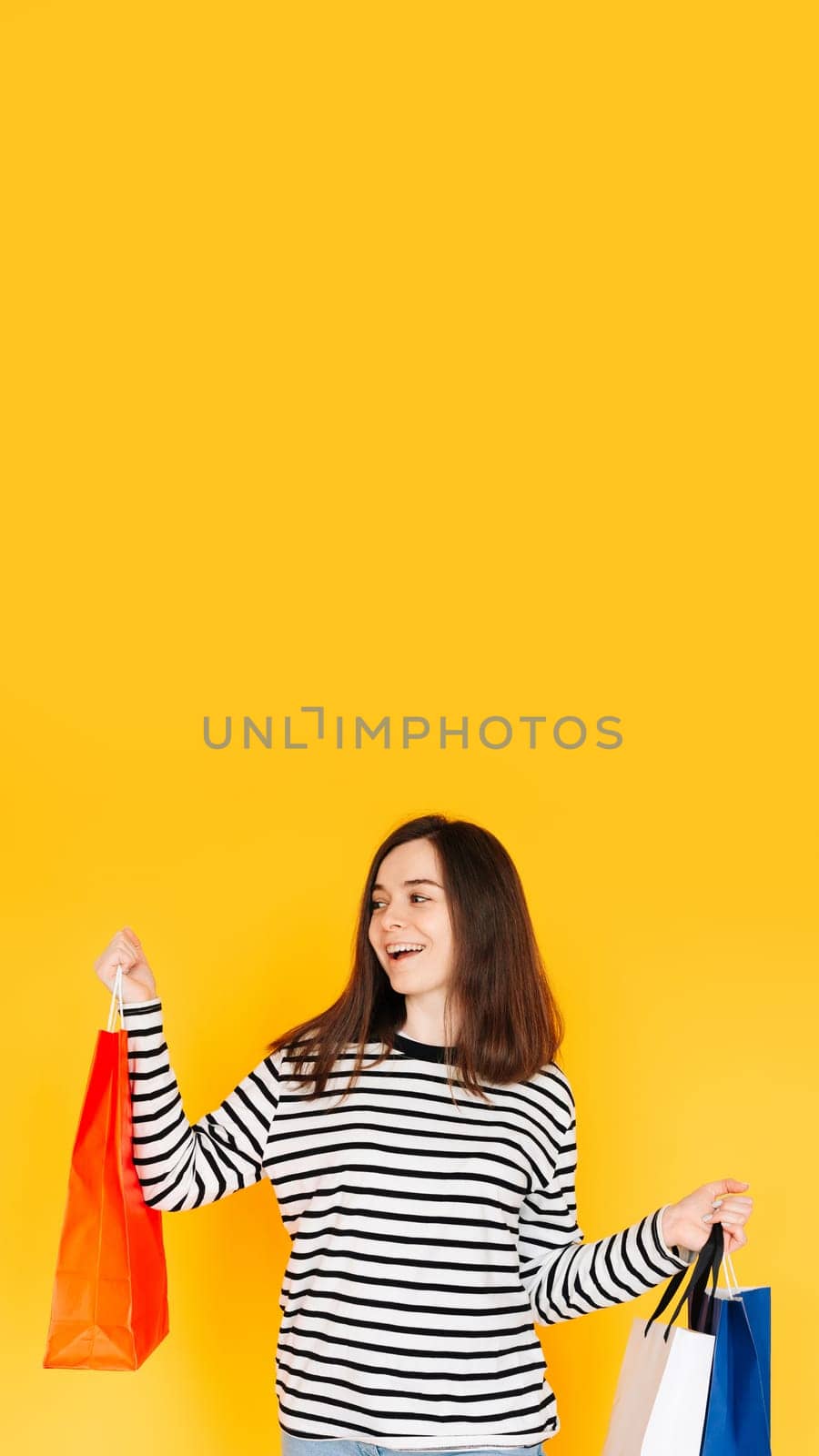 Delighted Shopper Concept: Captivating Woman Excited About Bargains and Discounts, Looking at Empty Space - Shopping Spree Mood Isolated on Vibrant Yellow Background by ViShark