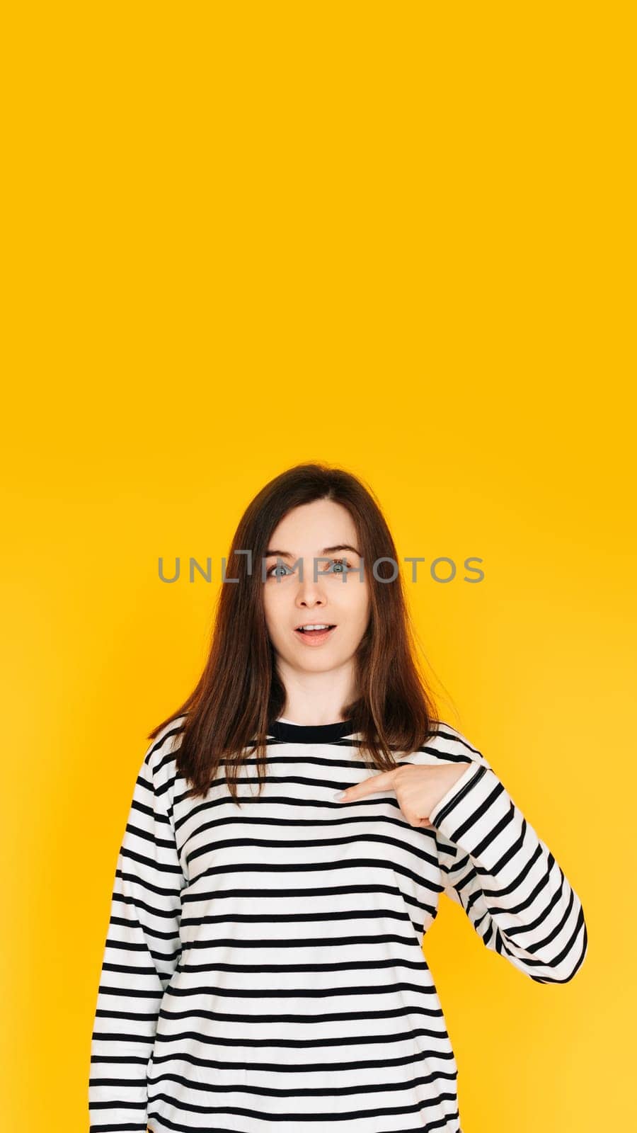 Delighted Woman Pointing at Herself in Amazement - Humorous Reaction Concept on Bright Yellow Background. Surprised and Amused Woman Pointing at Herself with Open Mouth - Self-Recognition Humor.