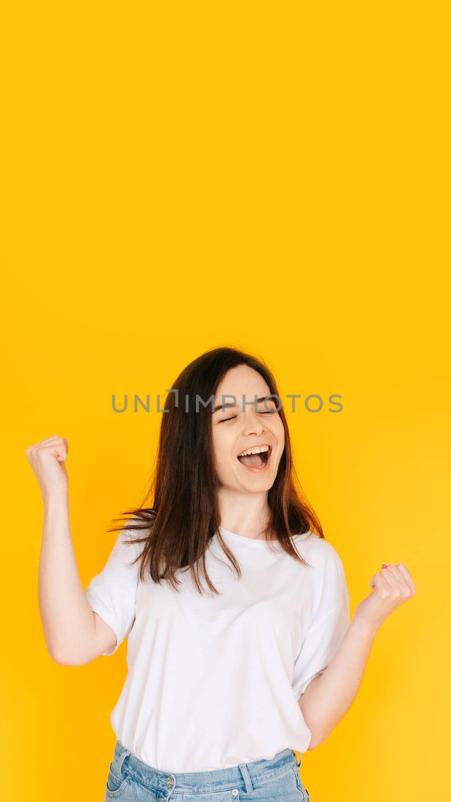 Exultant Woman Celebrating with Fist Raised, Shouting 'Yes' - Victory, Achievement, Success Concept on Vibrant Yellow Background.