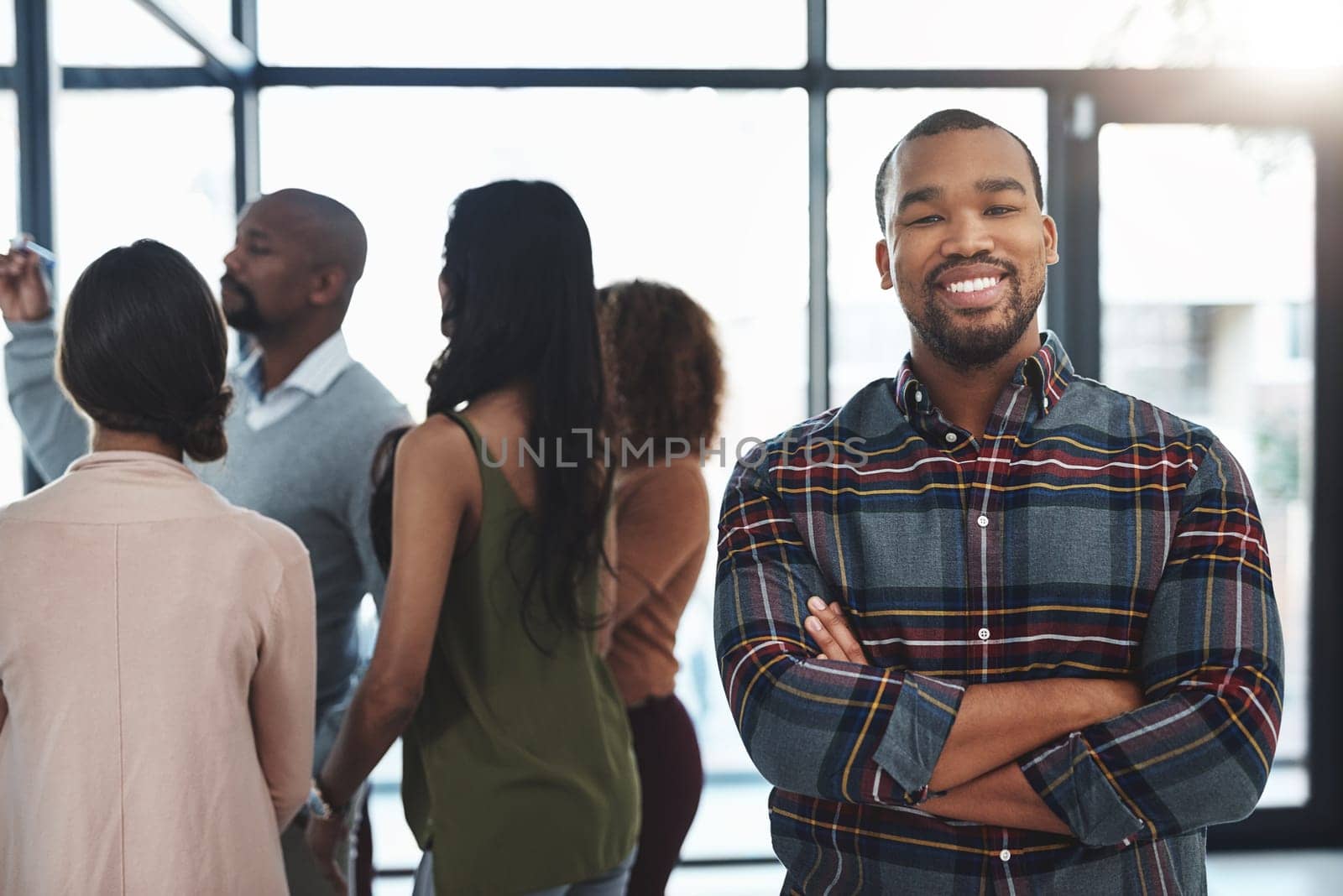 Im confident in my team. Portrait of a handsome young man standing in the office with his colleagues in the background. by YuriArcurs