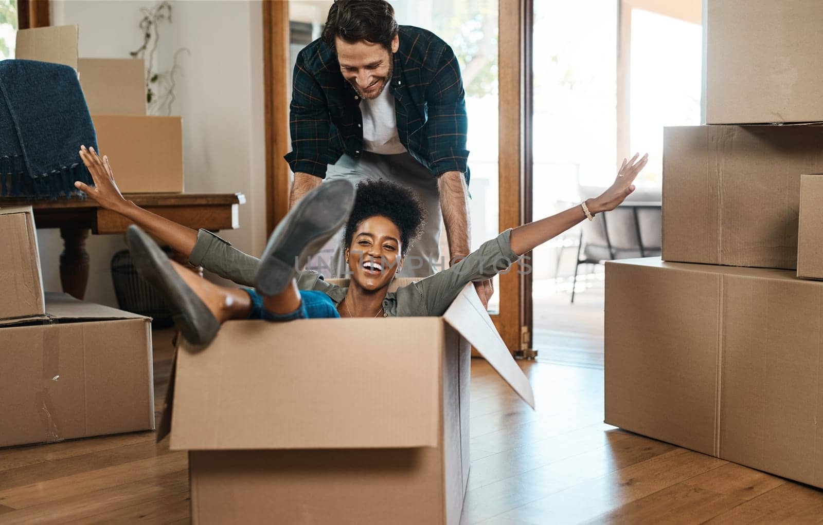 Happy couple, box and fun for moving to new home, real estate property and celebrate together. Excited man, woman and interracial partner playing in boxes at house for freedom, renovation or mortgage.