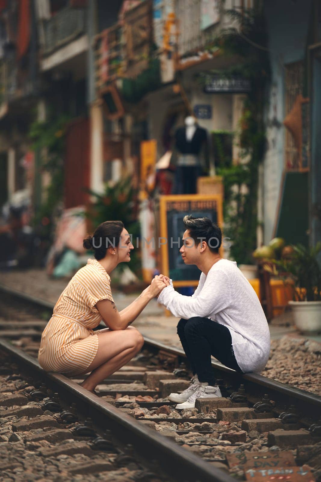 Id travel the whole world to see you. a young couple sharing a romantic moment on the train tracks in the streets of Vietnam. by YuriArcurs