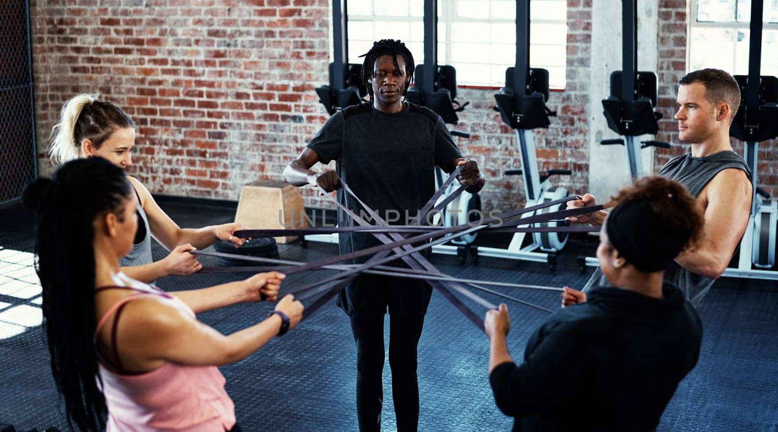 Adding variety to your workouts is a good thing. a fitness group working out with resistance bands in their session at the gym