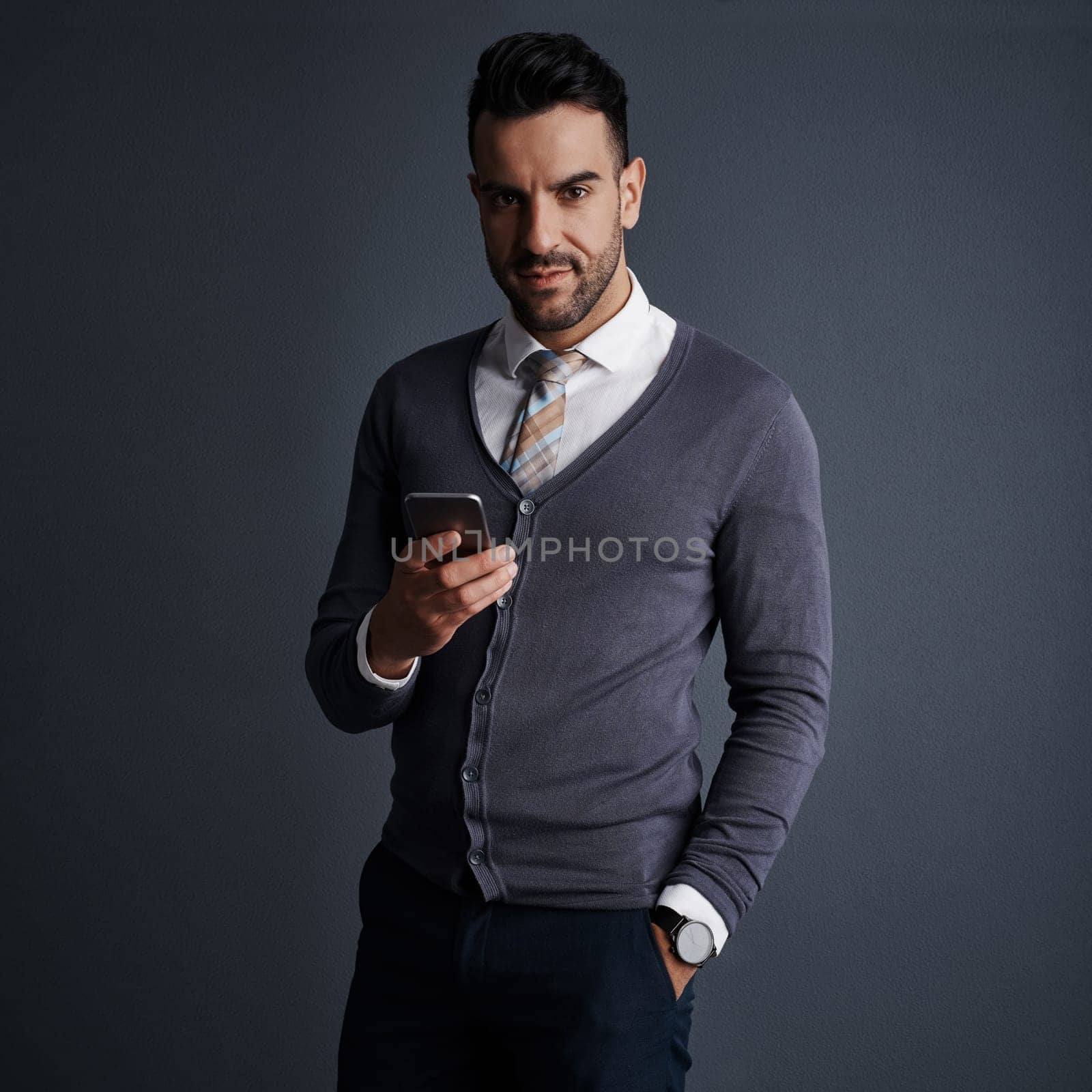 Availability is the key to my success. Studio shot of a stylish young businessman using a mobile phone against a gray background. by YuriArcurs