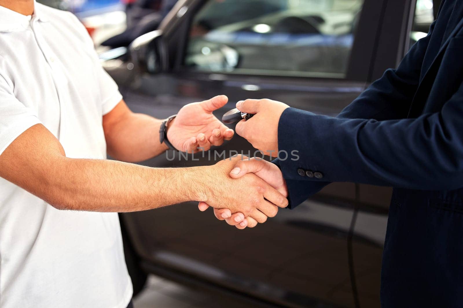 Car dealership, man hands and handshake from purchase and loan deal at motor showroom with salesman. Male person with shaking hands from agreement, payment success and contract with a transport sale.