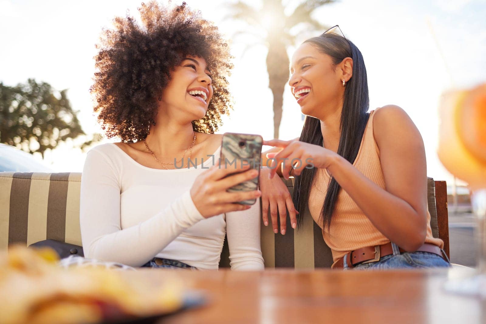Laughing, happy and women with a phone at a cafe for a meme or social media notification. Smile, talking and friends with a mobile for a funny app, comic conversation or comedy together at restaurant by YuriArcurs