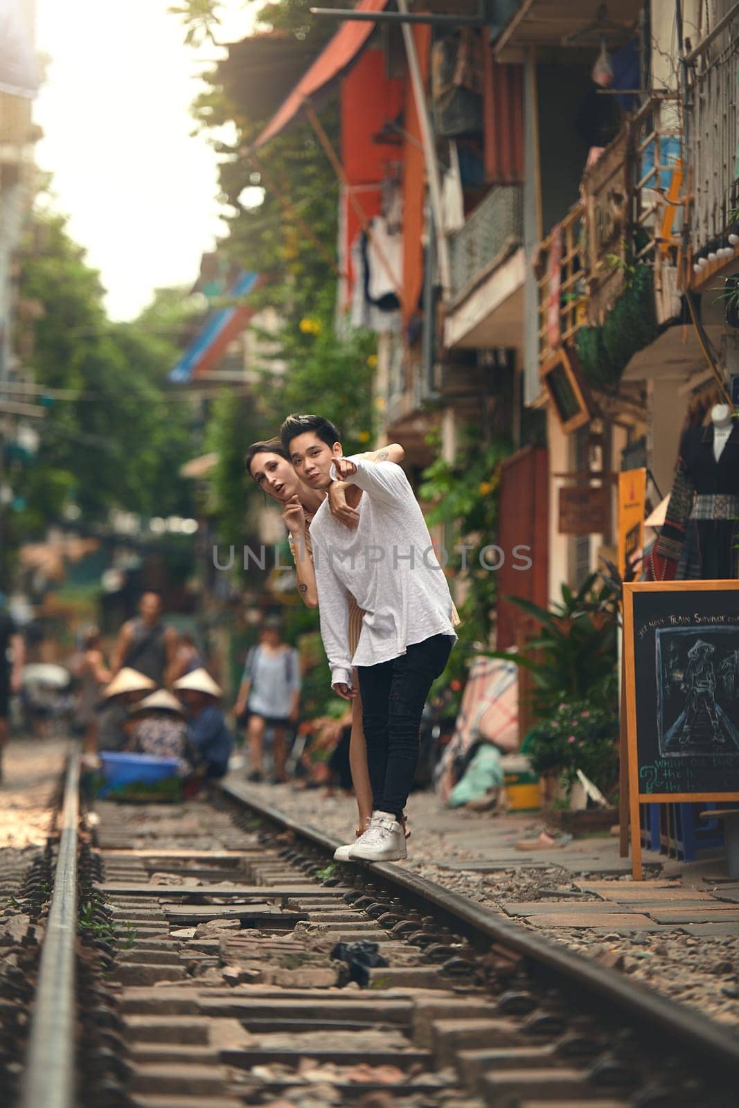 One day our train will come in. a young couple waiting for their train to arrive while exploring Vietnam. by YuriArcurs