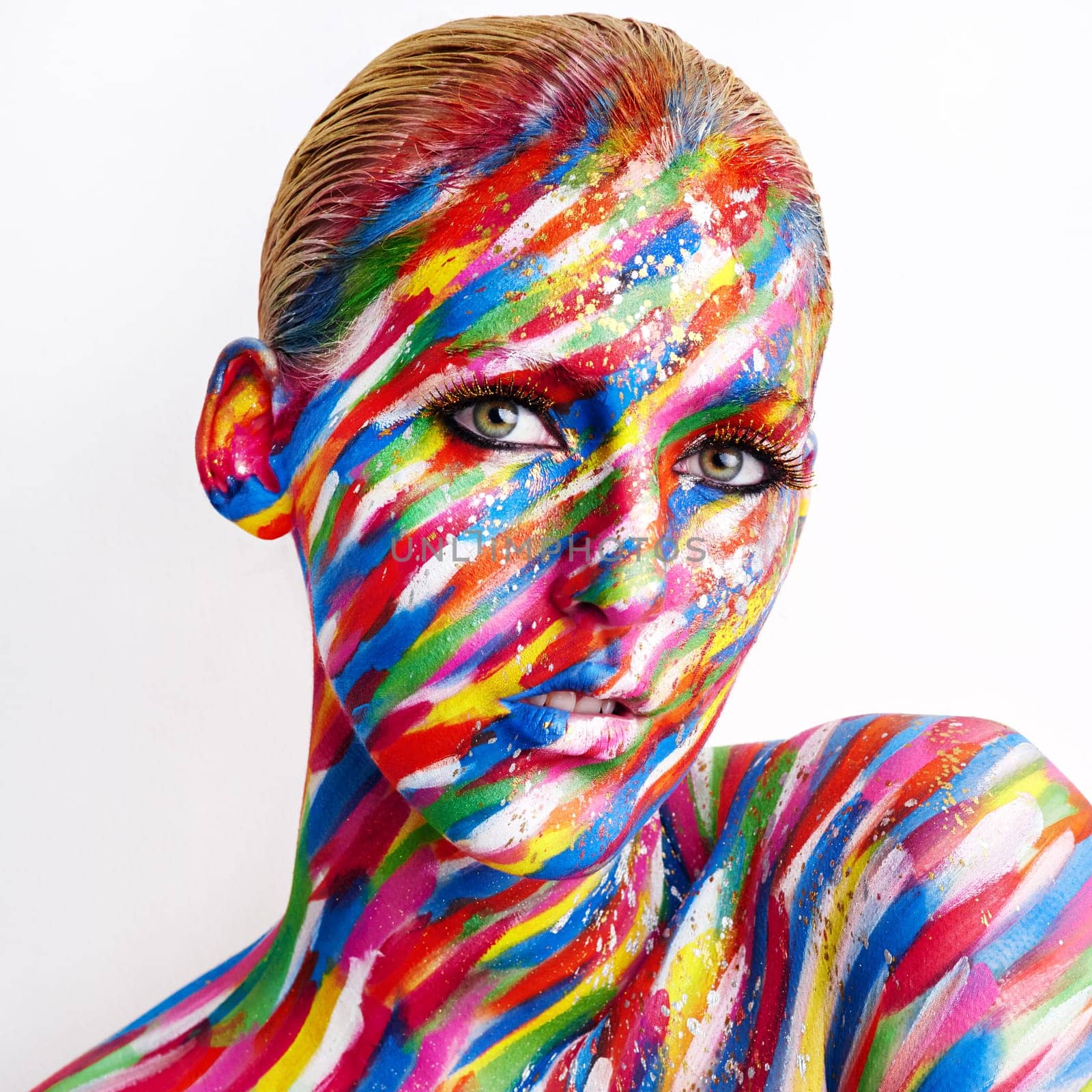 Bold is beautiful. Studio shot of a young woman posing with brightly colored paint on her face against a white background. by YuriArcurs