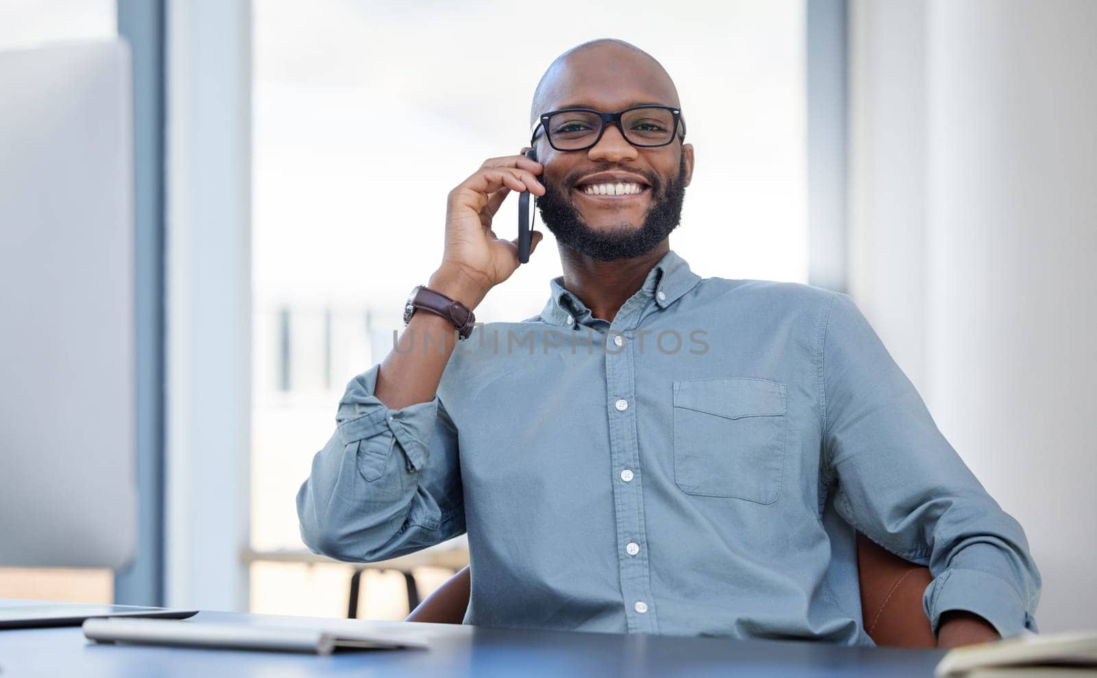 Smile, portrait of a businessman with cellphone and on a phone call in his workplace office. Online communication, happy and African man with smartphone talking at his modern workspace at desk by YuriArcurs