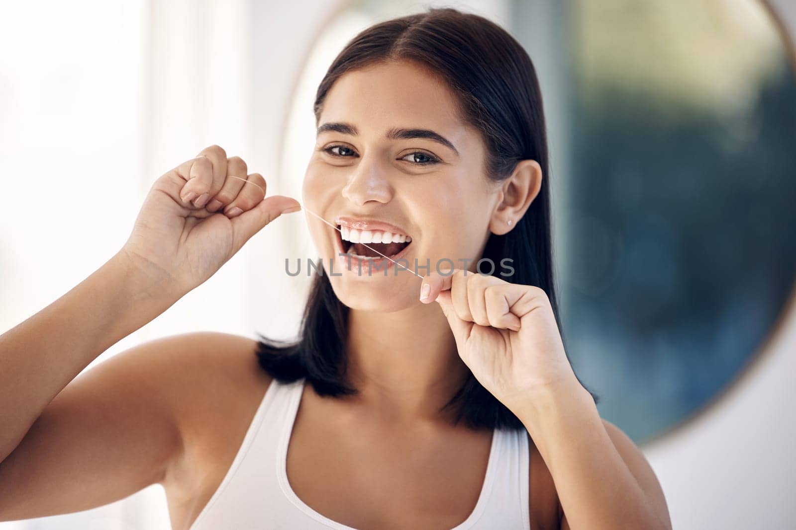 Smile, woman in bathroom flossing teeth and morning dental care routine in home mirror. Health, wellness and Indian woman with dental floss, motivation for cleaning for healthy mouth and fresh breath by YuriArcurs
