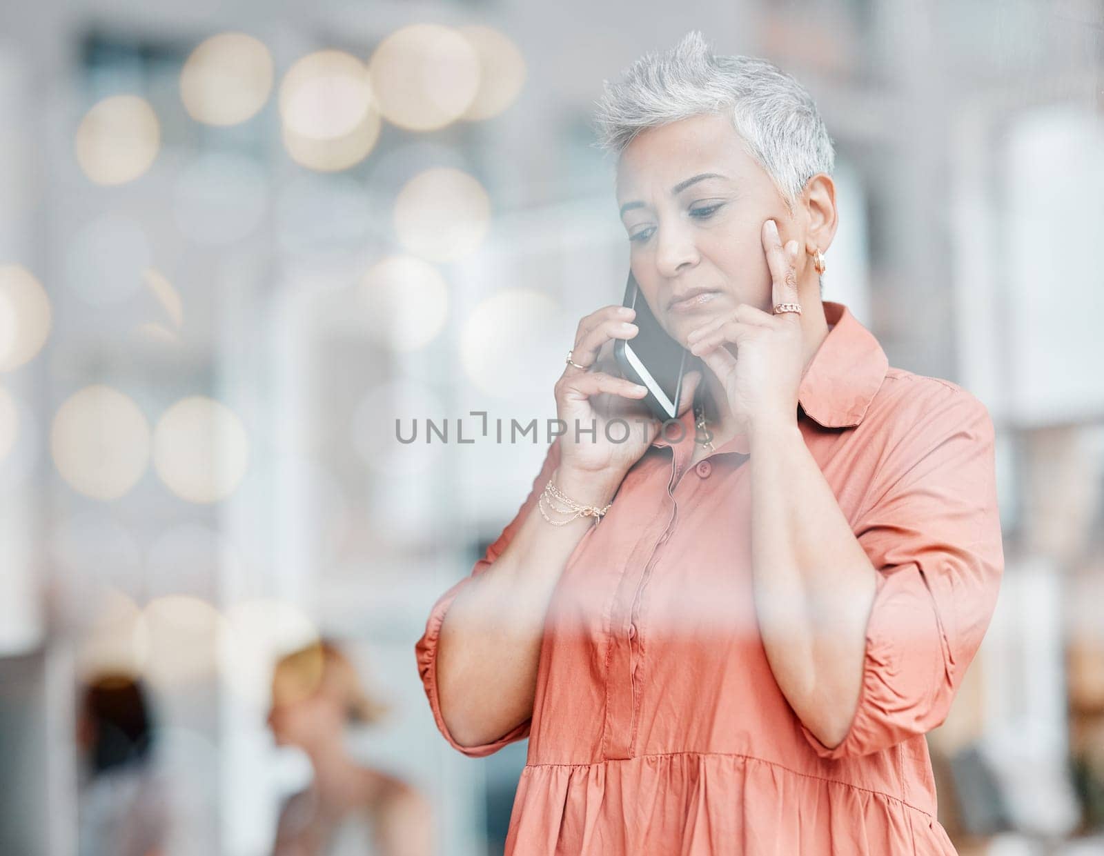 Phone call, sad and senior business woman talking, chatting or speaking in workplace. Bokeh window, communication and elderly female with depression, networking or discussion on mobile smartphone. by YuriArcurs