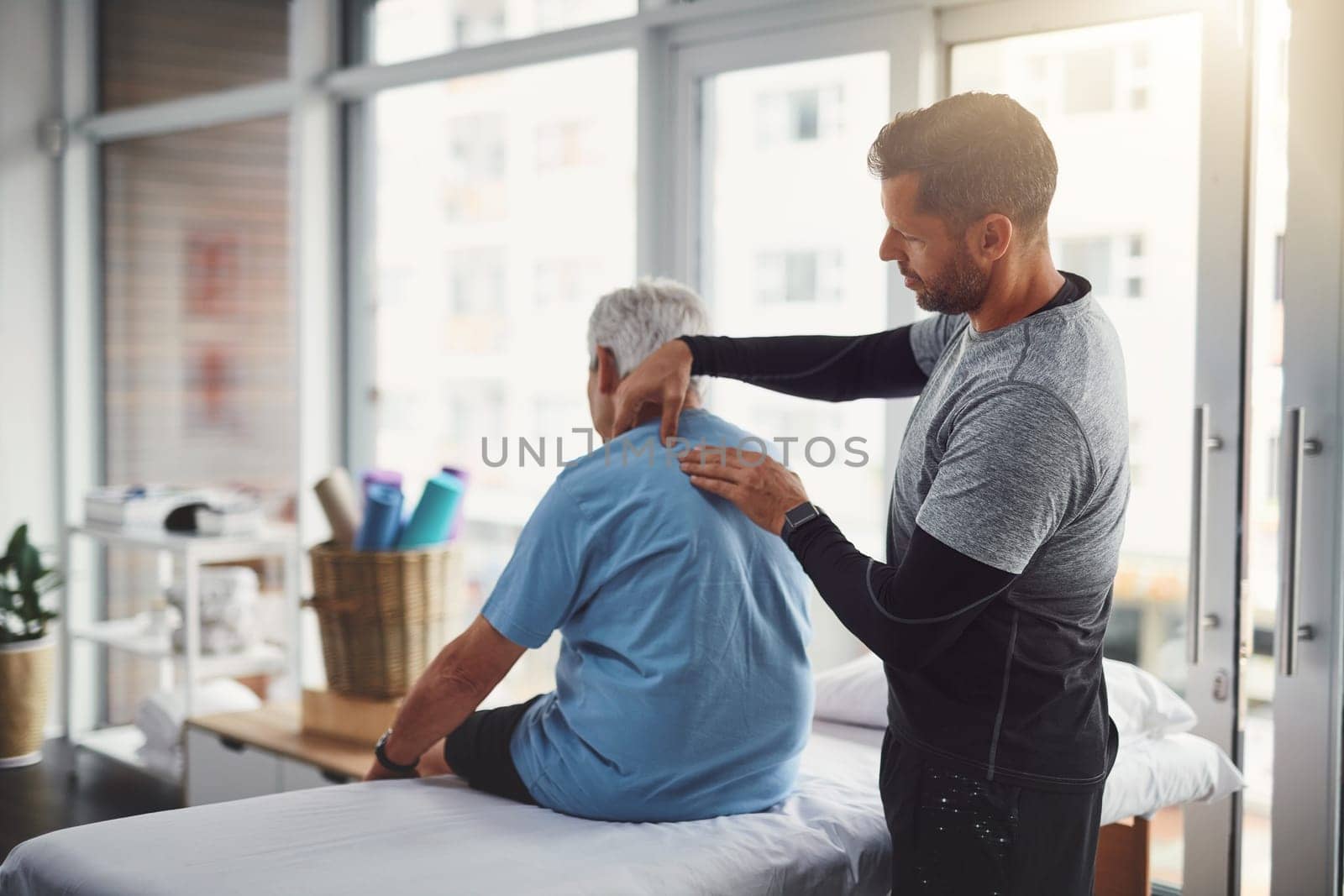 Are you feeling any discomfort over here. a young male physiotherapist assisting a senior patient in recovery. by YuriArcurs