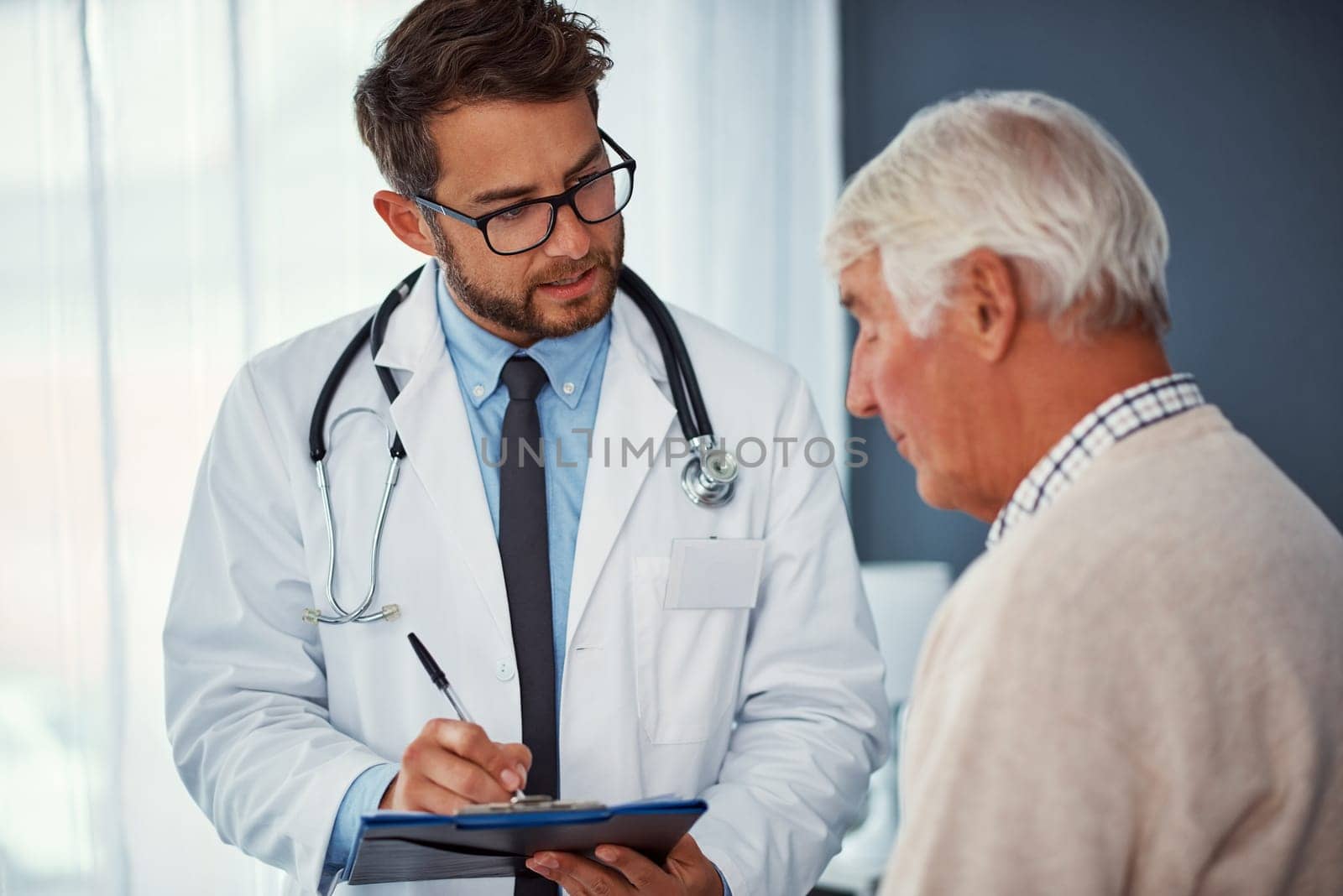 Tell me more about the pain youve been feeling...a doctor writing notes while examining a senior patient in a clinic