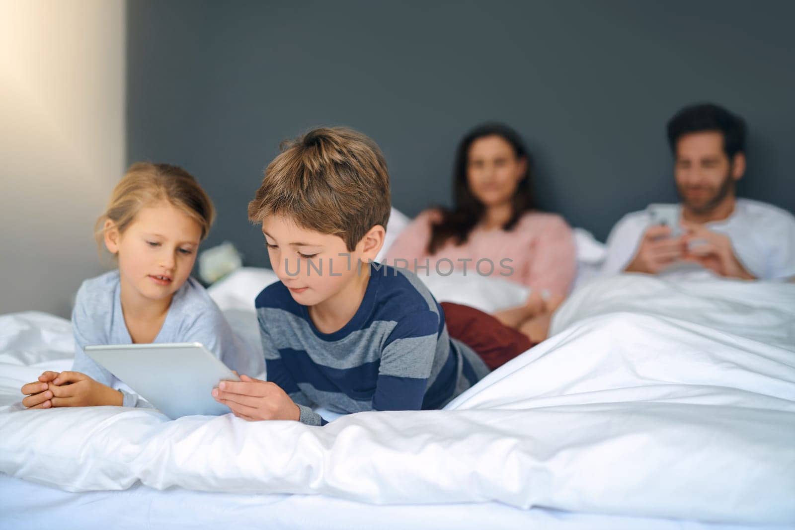 Mornings in our home. an adorable little girl and boy using a tablet together while their parents are chilling in bed at home