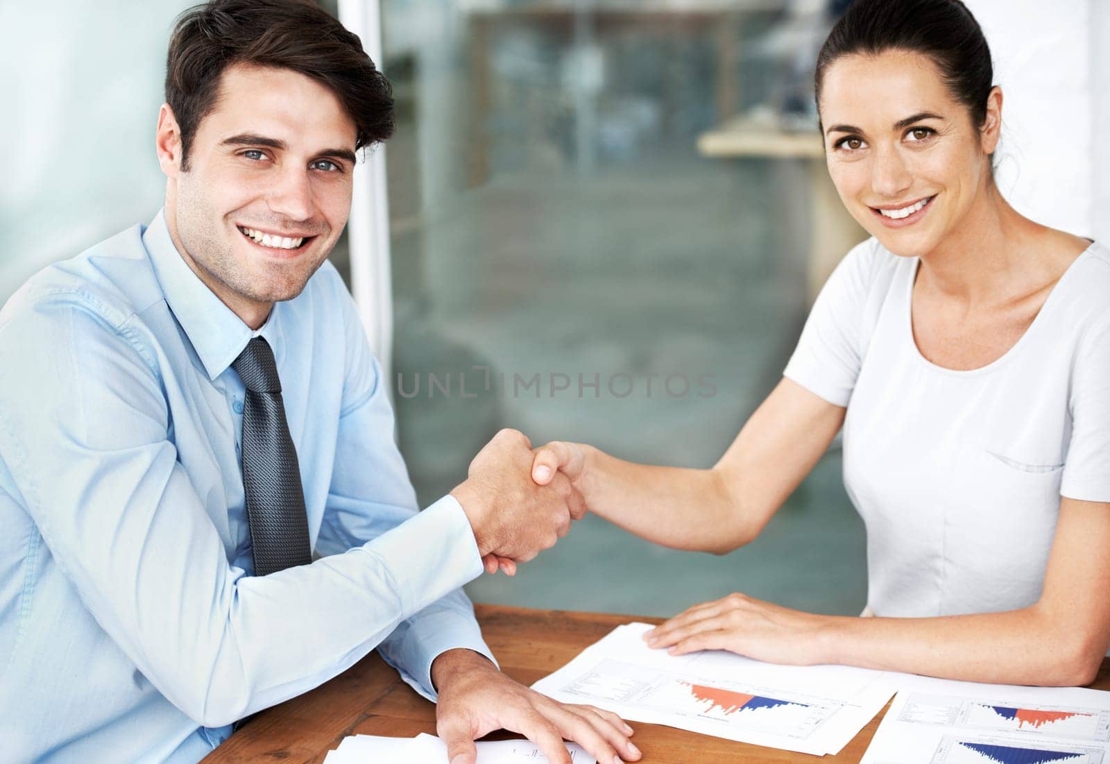 Working in complete synergy. Young businesspeople shaking hands while seated at a desk. by YuriArcurs