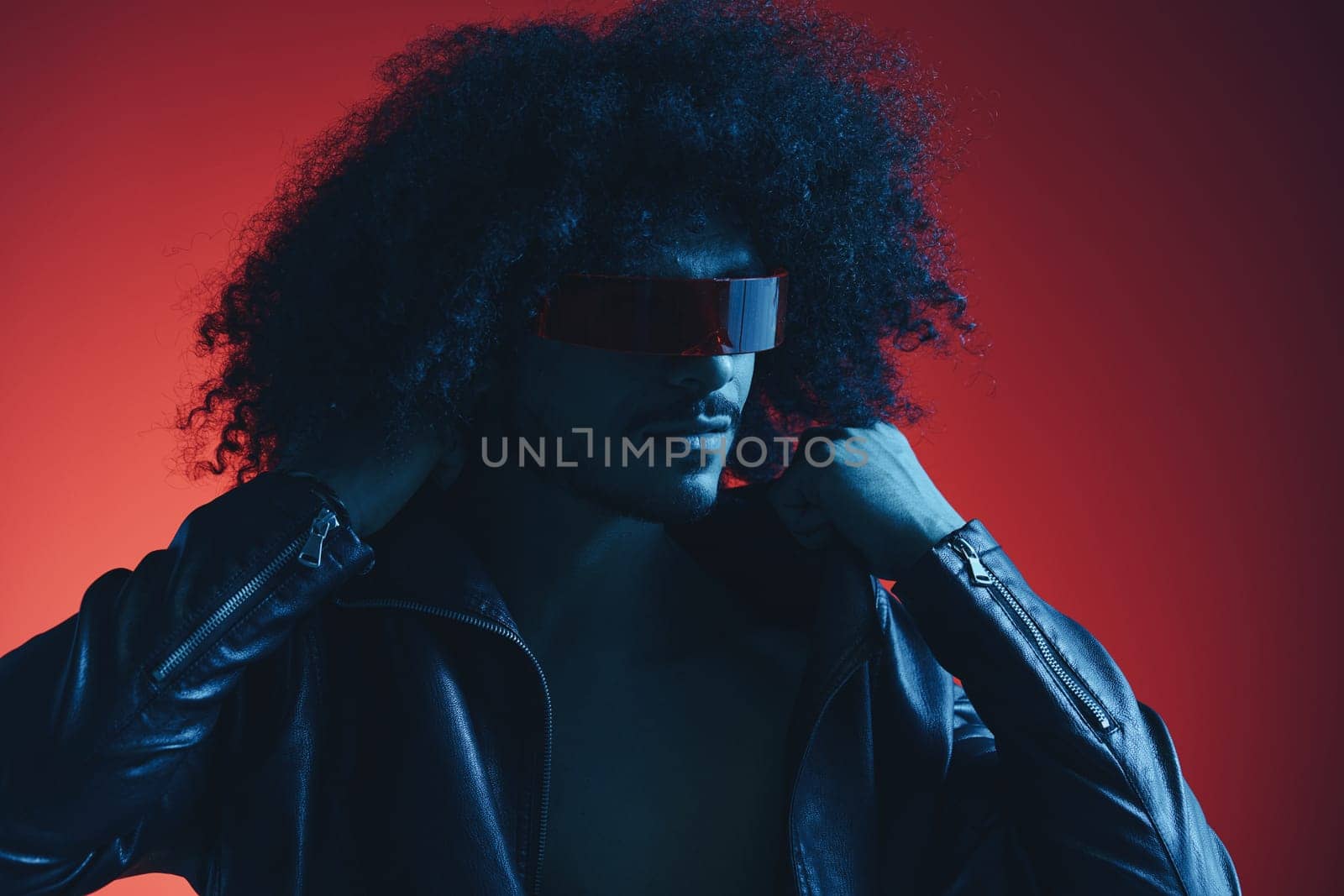 Portrait of fashion man with curly hair on red background with stylish glasses, multicultural, colored light, black leather jacket trend, modern concept. by SHOTPRIME