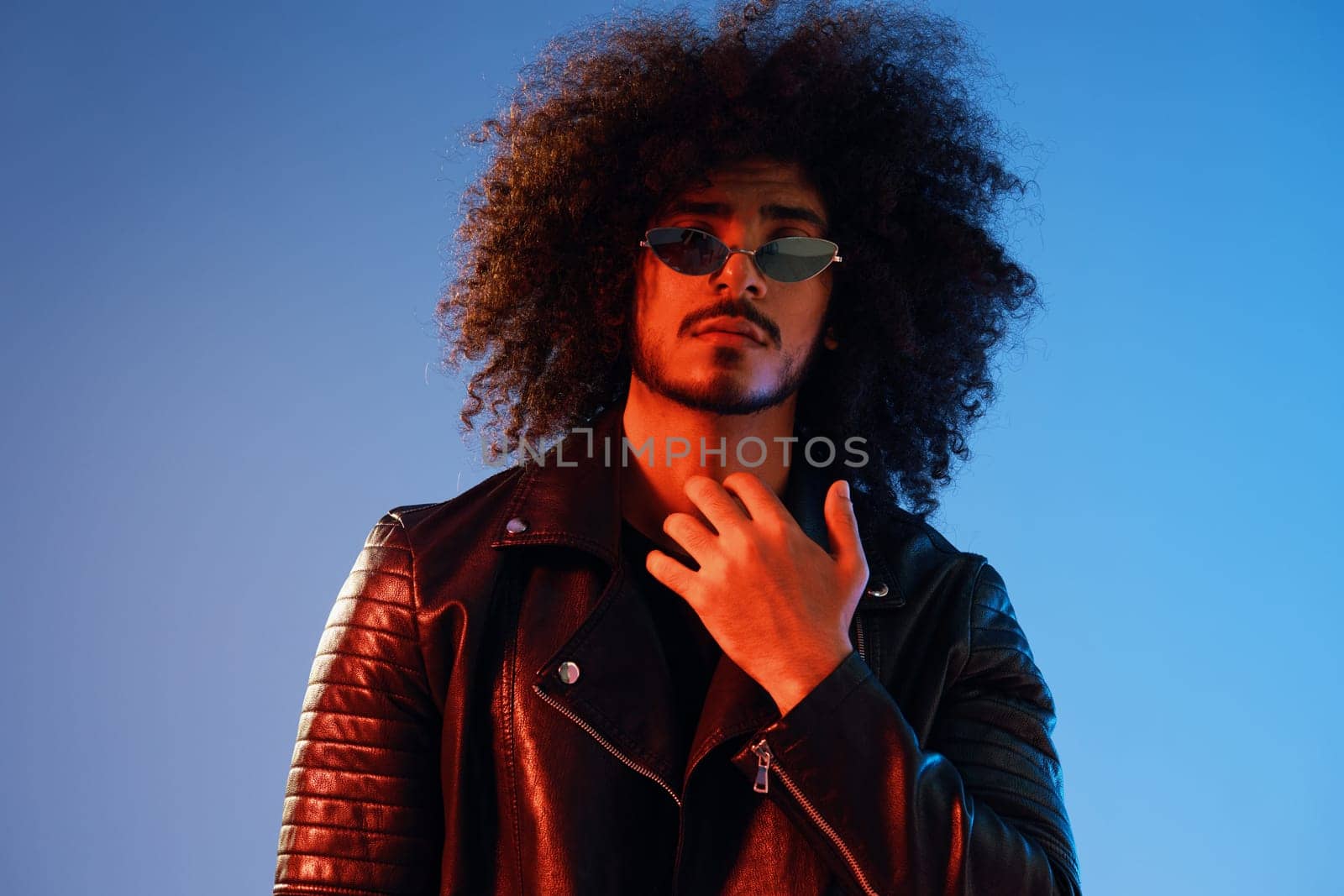 Portrait of a stylish man with curly hair on a blue background multinational, colored light, trendy glasses, modern concept. by SHOTPRIME