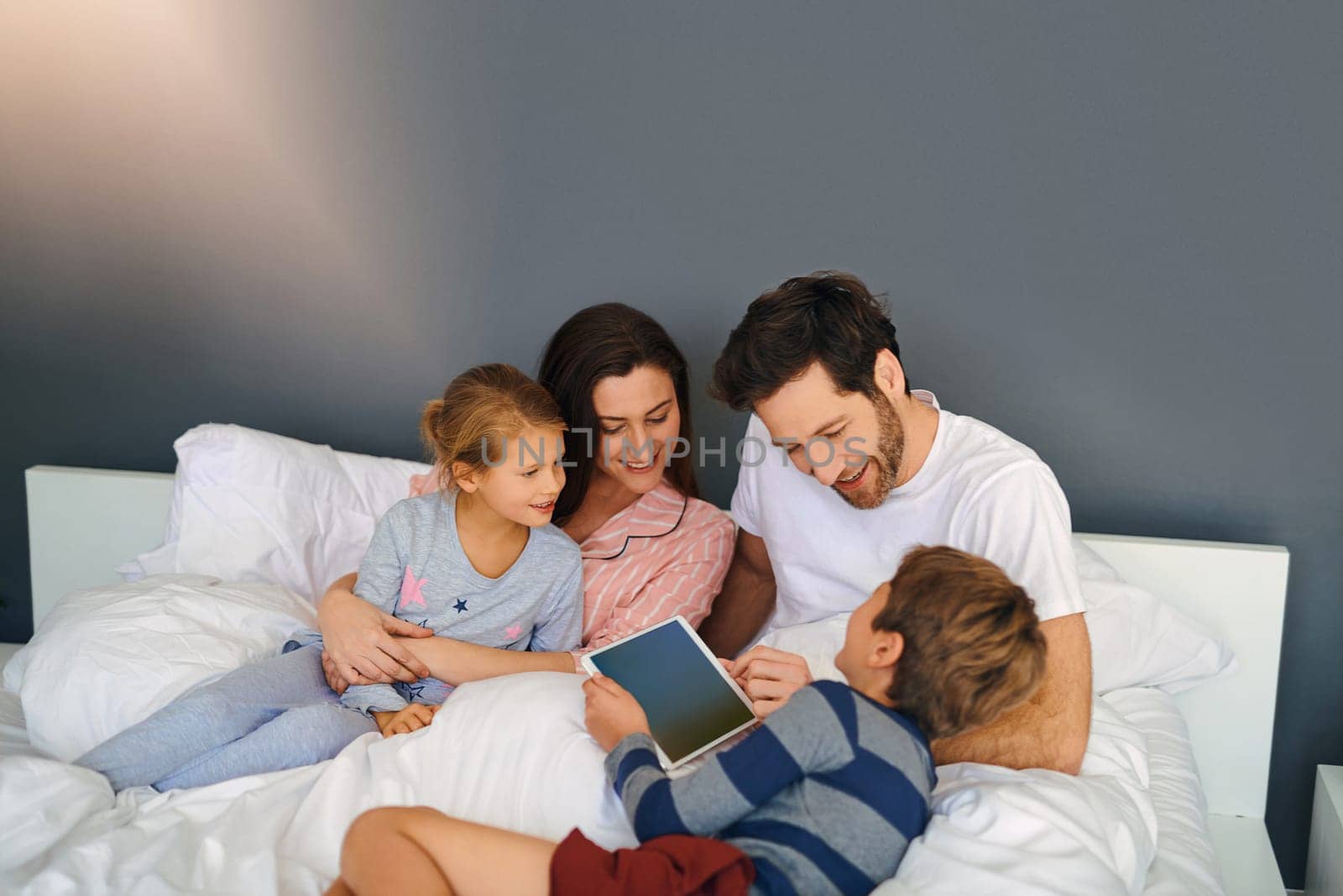 They sure do love watching shows together. a young family using a tablet while chilling in bed together at home. by YuriArcurs