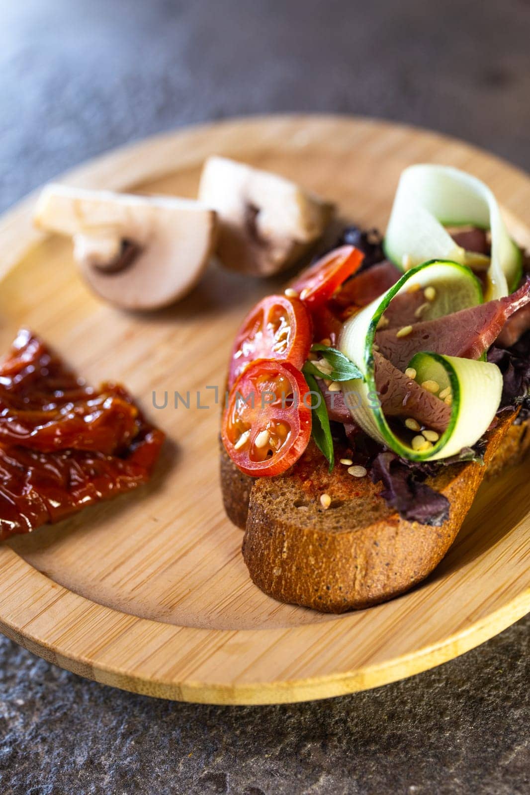 close-up of black bread bruschetta with tomato and cucumber on a wooden plate by Pukhovskiy